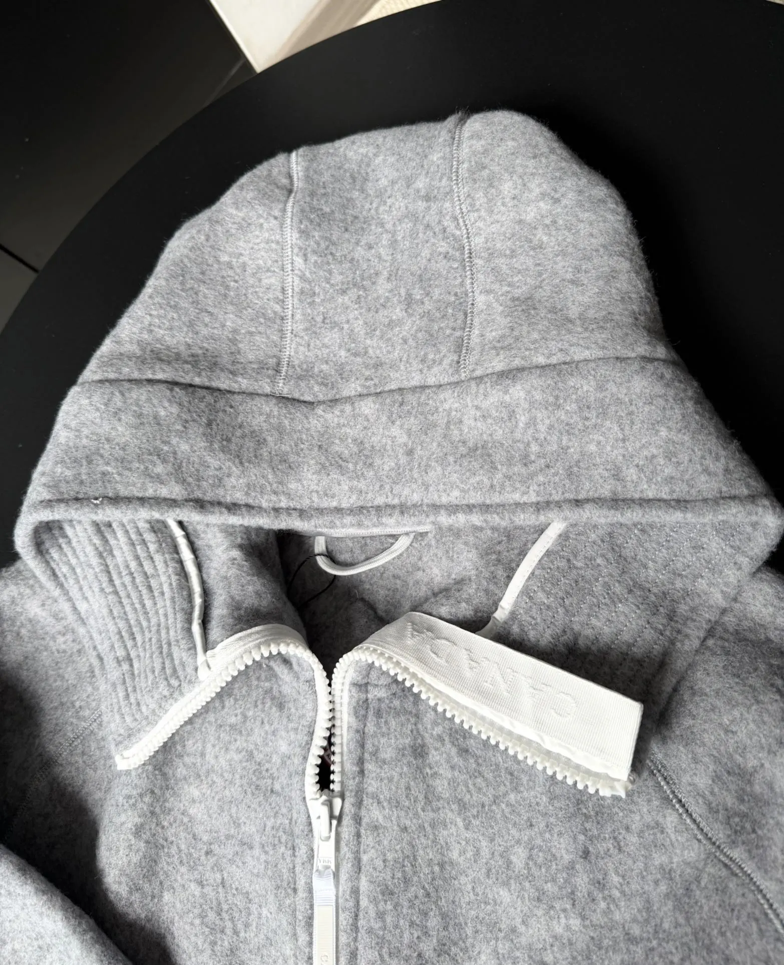 大鹅/Canada Goose抓绒羊毛饰章连帽夹克外套 面料选择: 以羊毛为主体，加入极少量氨纶和聚酯纤维混纺而成的羊毛抓绒面料。羊毛作为核心天然成分，提供无与伦比的温度调节、抑菌防臭和亲肤感。少量氨纶的喂入赋予了面料一定的四向弹性，日常活动时毫无束缚感。作为抓绒结构的基础，聚酯纤维增强了面料的耐久性、抗皱性和快干性，它构成了抓绒的蓬松感，并提供锁住空气等功能。 细节1: 衣袖和下摆采用2乘2罗纹收口，其强大的弹性，可以紧密贴合不同粗细的手腕和腰部，形成一个有效的&lsquo;密封&rsquo;,防止冷风倒灌。在多次拉伸和使用后仍能保持原有形状，不易松垮变形。且罗纹袖口能传递一种设计感，强化视觉美观度。 细节2: 兜帽设计与松紧扣的搭配提升穿戴时的保暖度与防风性能。 辅料:定制弹性抽绳松紧扣定制拉链吊坠定制臂章 尺码：S M L 颜色：黑 灰 咖 米 粉