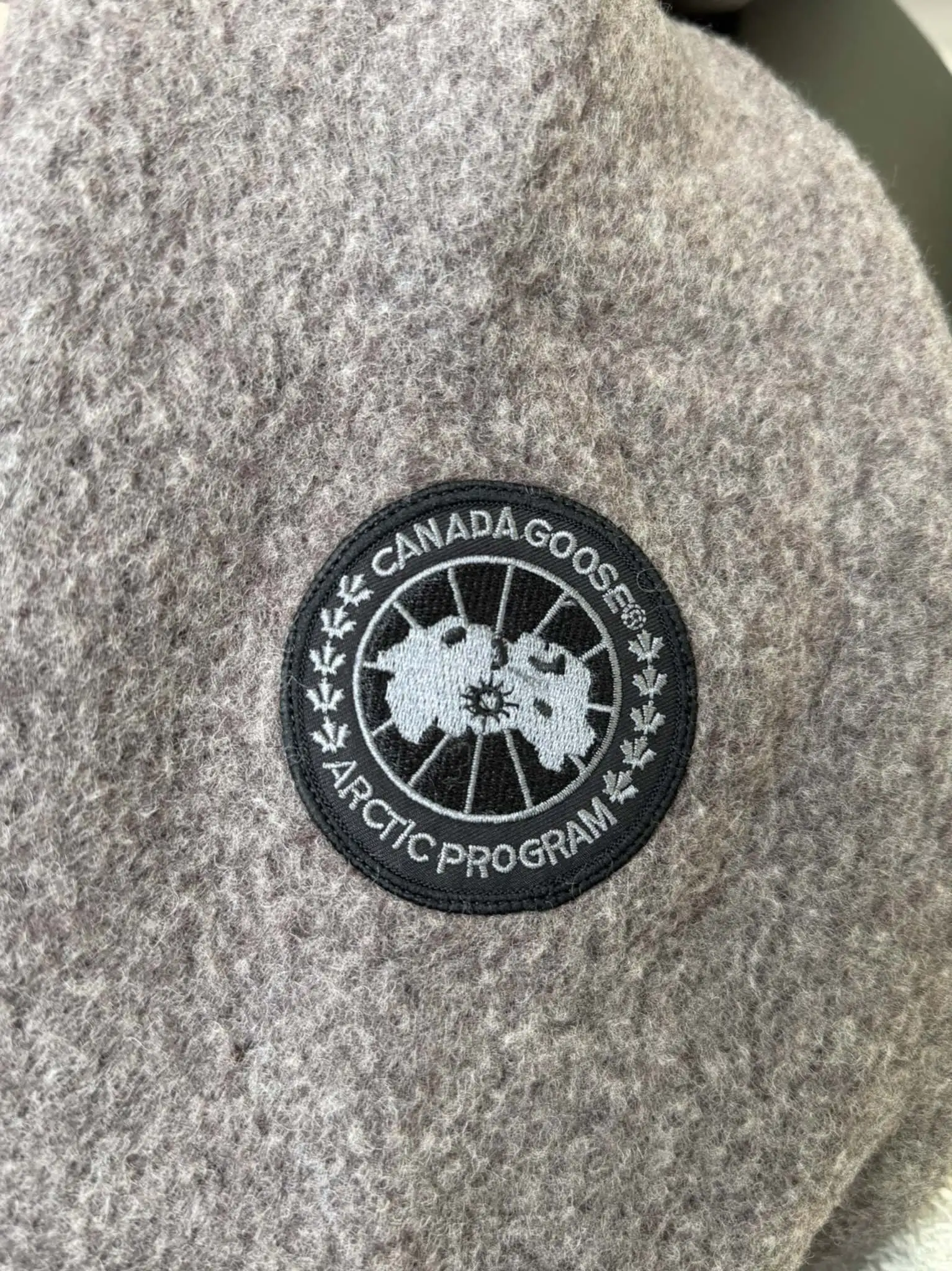 大鹅/Canada Goose抓绒羊毛饰章连帽夹克外套 面料选择: 以羊毛为主体，加入极少量氨纶和聚酯纤维混纺而成的羊毛抓绒面料。羊毛作为核心天然成分，提供无与伦比的温度调节、抑菌防臭和亲肤感。少量氨纶的喂入赋予了面料一定的四向弹性，日常活动时毫无束缚感。作为抓绒结构的基础，聚酯纤维增强了面料的耐久性、抗皱性和快干性，它构成了抓绒的蓬松感，并提供锁住空气等功能。 细节1: 衣袖和下摆采用2乘2罗纹收口，其强大的弹性，可以紧密贴合不同粗细的手腕和腰部，形成一个有效的&lsquo;密封&rsquo;,防止冷风倒灌。在多次拉伸和使用后仍能保持原有形状，不易松垮变形。且罗纹袖口能传递一种设计感，强化视觉美观度。 细节2: 兜帽设计与松紧扣的搭配提升穿戴时的保暖度与防风性能。 辅料:定制弹性抽绳松紧扣定制拉链吊坠定制臂章 尺码：S M L 颜色：黑 灰 咖 米 粉