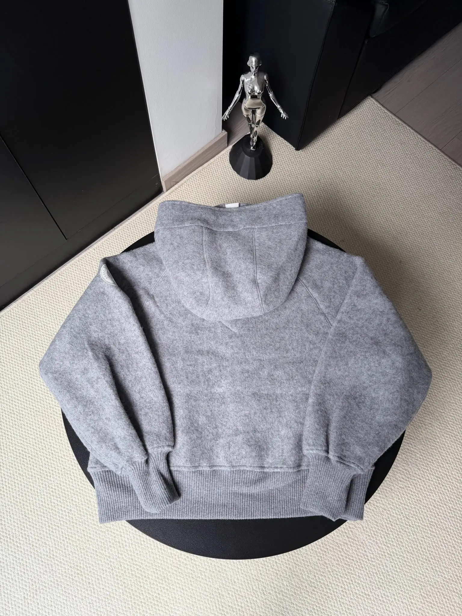 大鹅/Canada Goose抓绒羊毛饰章连帽夹克外套 面料选择: 以羊毛为主体，加入极少量氨纶和聚酯纤维混纺而成的羊毛抓绒面料。羊毛作为核心天然成分，提供无与伦比的温度调节、抑菌防臭和亲肤感。少量氨纶的喂入赋予了面料一定的四向弹性，日常活动时毫无束缚感。作为抓绒结构的基础，聚酯纤维增强了面料的耐久性、抗皱性和快干性，它构成了抓绒的蓬松感，并提供锁住空气等功能。 细节1: 衣袖和下摆采用2乘2罗纹收口，其强大的弹性，可以紧密贴合不同粗细的手腕和腰部，形成一个有效的&lsquo;密封&rsquo;,防止冷风倒灌。在多次拉伸和使用后仍能保持原有形状，不易松垮变形。且罗纹袖口能传递一种设计感，强化视觉美观度。 细节2: 兜帽设计与松紧扣的搭配提升穿戴时的保暖度与防风性能。 辅料:定制弹性抽绳松紧扣定制拉链吊坠定制臂章 尺码：S M L 颜色：黑 灰 咖 米 粉