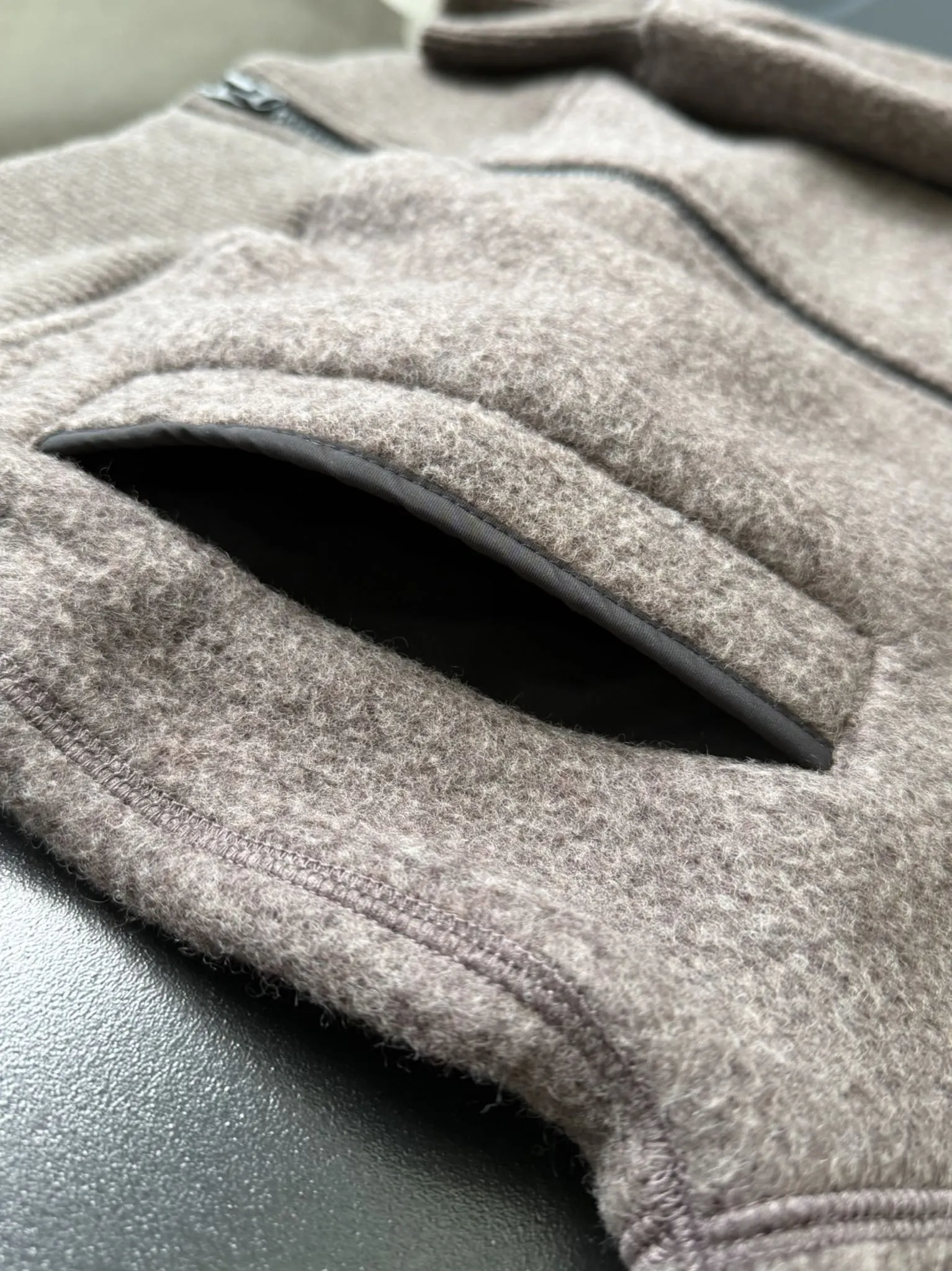 大鹅/Canada Goose抓绒羊毛饰章连帽夹克外套 面料选择: 以羊毛为主体，加入极少量氨纶和聚酯纤维混纺而成的羊毛抓绒面料。羊毛作为核心天然成分，提供无与伦比的温度调节、抑菌防臭和亲肤感。少量氨纶的喂入赋予了面料一定的四向弹性，日常活动时毫无束缚感。作为抓绒结构的基础，聚酯纤维增强了面料的耐久性、抗皱性和快干性，它构成了抓绒的蓬松感，并提供锁住空气等功能。 细节1: 衣袖和下摆采用2乘2罗纹收口，其强大的弹性，可以紧密贴合不同粗细的手腕和腰部，形成一个有效的&lsquo;密封&rsquo;,防止冷风倒灌。在多次拉伸和使用后仍能保持原有形状，不易松垮变形。且罗纹袖口能传递一种设计感，强化视觉美观度。 细节2: 兜帽设计与松紧扣的搭配提升穿戴时的保暖度与防风性能。 辅料:定制弹性抽绳松紧扣定制拉链吊坠定制臂章 尺码：S M L 颜色：黑 灰 咖 米 粉