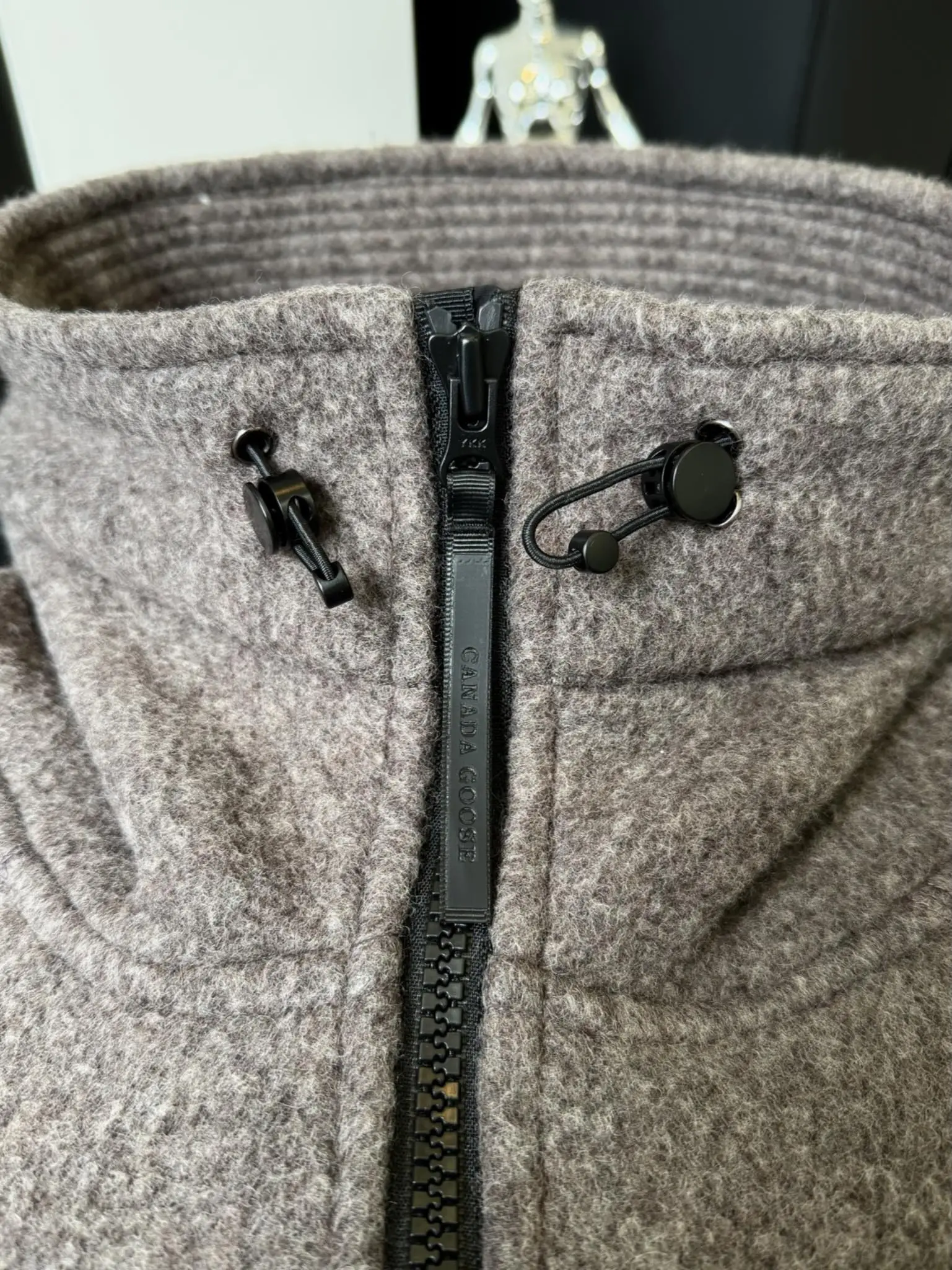 大鹅/Canada Goose抓绒羊毛饰章连帽夹克外套 面料选择: 以羊毛为主体，加入极少量氨纶和聚酯纤维混纺而成的羊毛抓绒面料。羊毛作为核心天然成分，提供无与伦比的温度调节、抑菌防臭和亲肤感。少量氨纶的喂入赋予了面料一定的四向弹性，日常活动时毫无束缚感。作为抓绒结构的基础，聚酯纤维增强了面料的耐久性、抗皱性和快干性，它构成了抓绒的蓬松感，并提供锁住空气等功能。 细节1: 衣袖和下摆采用2乘2罗纹收口，其强大的弹性，可以紧密贴合不同粗细的手腕和腰部，形成一个有效的&lsquo;密封&rsquo;,防止冷风倒灌。在多次拉伸和使用后仍能保持原有形状，不易松垮变形。且罗纹袖口能传递一种设计感，强化视觉美观度。 细节2: 兜帽设计与松紧扣的搭配提升穿戴时的保暖度与防风性能。 辅料:定制弹性抽绳松紧扣定制拉链吊坠定制臂章 尺码：S M L 颜色：黑 灰 咖 米 粉