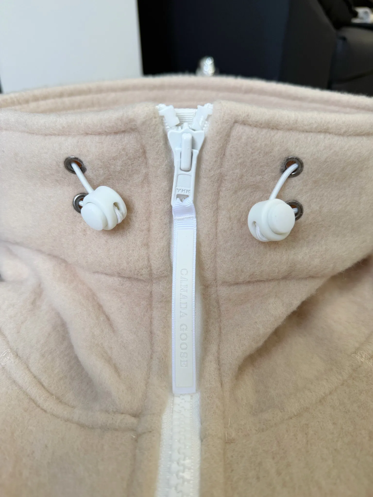 大鹅/Canada Goose抓绒羊毛饰章连帽夹克外套 面料选择: 以羊毛为主体，加入极少量氨纶和聚酯纤维混纺而成的羊毛抓绒面料。羊毛作为核心天然成分，提供无与伦比的温度调节、抑菌防臭和亲肤感。少量氨纶的喂入赋予了面料一定的四向弹性，日常活动时毫无束缚感。作为抓绒结构的基础，聚酯纤维增强了面料的耐久性、抗皱性和快干性，它构成了抓绒的蓬松感，并提供锁住空气等功能。 细节1: 衣袖和下摆采用2乘2罗纹收口，其强大的弹性，可以紧密贴合不同粗细的手腕和腰部，形成一个有效的&lsquo;密封&rsquo;,防止冷风倒灌。在多次拉伸和使用后仍能保持原有形状，不易松垮变形。且罗纹袖口能传递一种设计感，强化视觉美观度。 细节2: 兜帽设计与松紧扣的搭配提升穿戴时的保暖度与防风性能。 辅料:定制弹性抽绳松紧扣定制拉链吊坠定制臂章 尺码：S M L 颜色：黑 灰 咖 米 粉