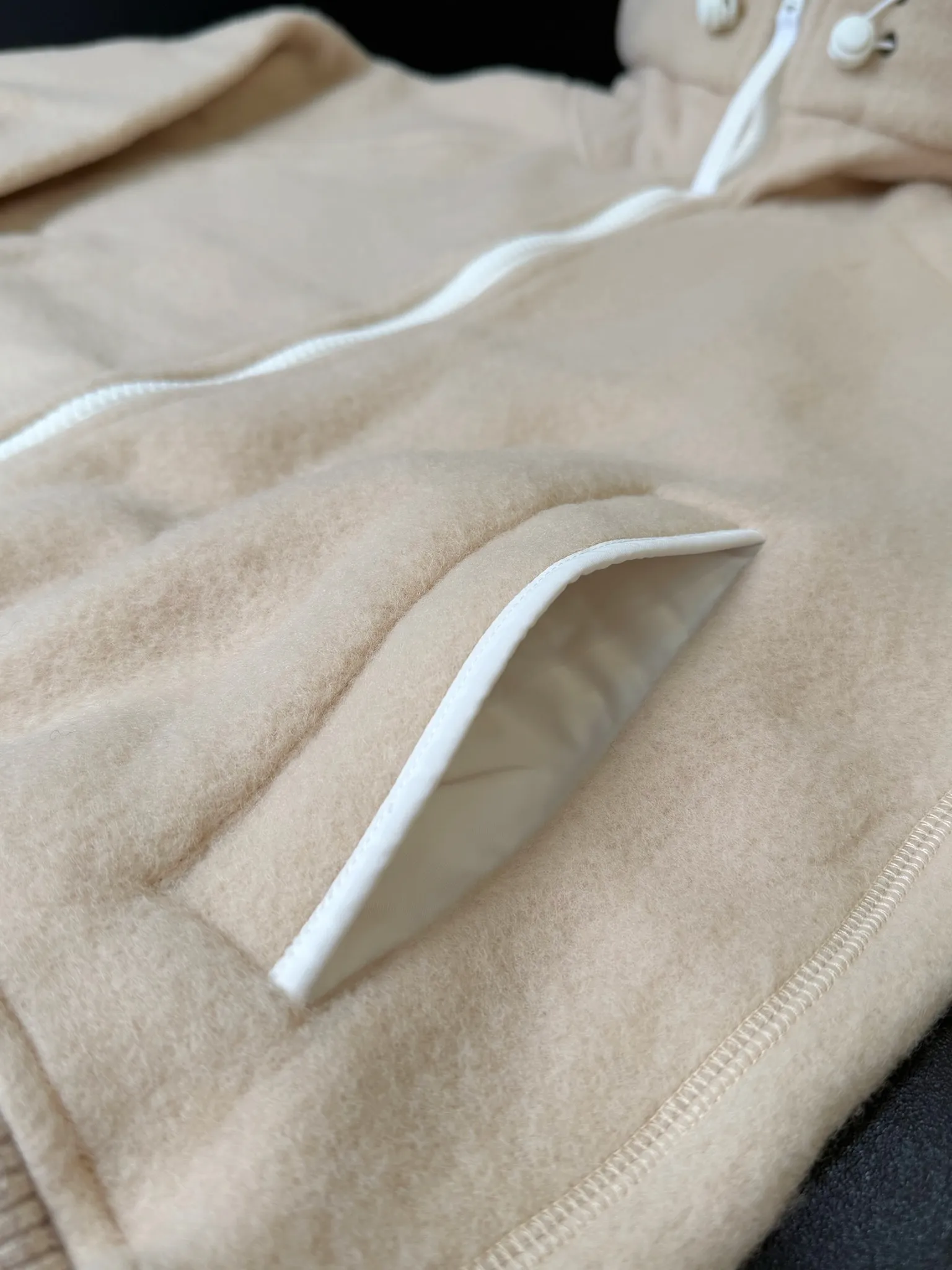 大鹅/Canada Goose抓绒羊毛饰章连帽夹克外套 面料选择: 以羊毛为主体，加入极少量氨纶和聚酯纤维混纺而成的羊毛抓绒面料。羊毛作为核心天然成分，提供无与伦比的温度调节、抑菌防臭和亲肤感。少量氨纶的喂入赋予了面料一定的四向弹性，日常活动时毫无束缚感。作为抓绒结构的基础，聚酯纤维增强了面料的耐久性、抗皱性和快干性，它构成了抓绒的蓬松感，并提供锁住空气等功能。 细节1: 衣袖和下摆采用2乘2罗纹收口，其强大的弹性，可以紧密贴合不同粗细的手腕和腰部，形成一个有效的&lsquo;密封&rsquo;,防止冷风倒灌。在多次拉伸和使用后仍能保持原有形状，不易松垮变形。且罗纹袖口能传递一种设计感，强化视觉美观度。 细节2: 兜帽设计与松紧扣的搭配提升穿戴时的保暖度与防风性能。 辅料:定制弹性抽绳松紧扣定制拉链吊坠定制臂章 尺码：S M L 颜色：黑 灰 咖 米 粉