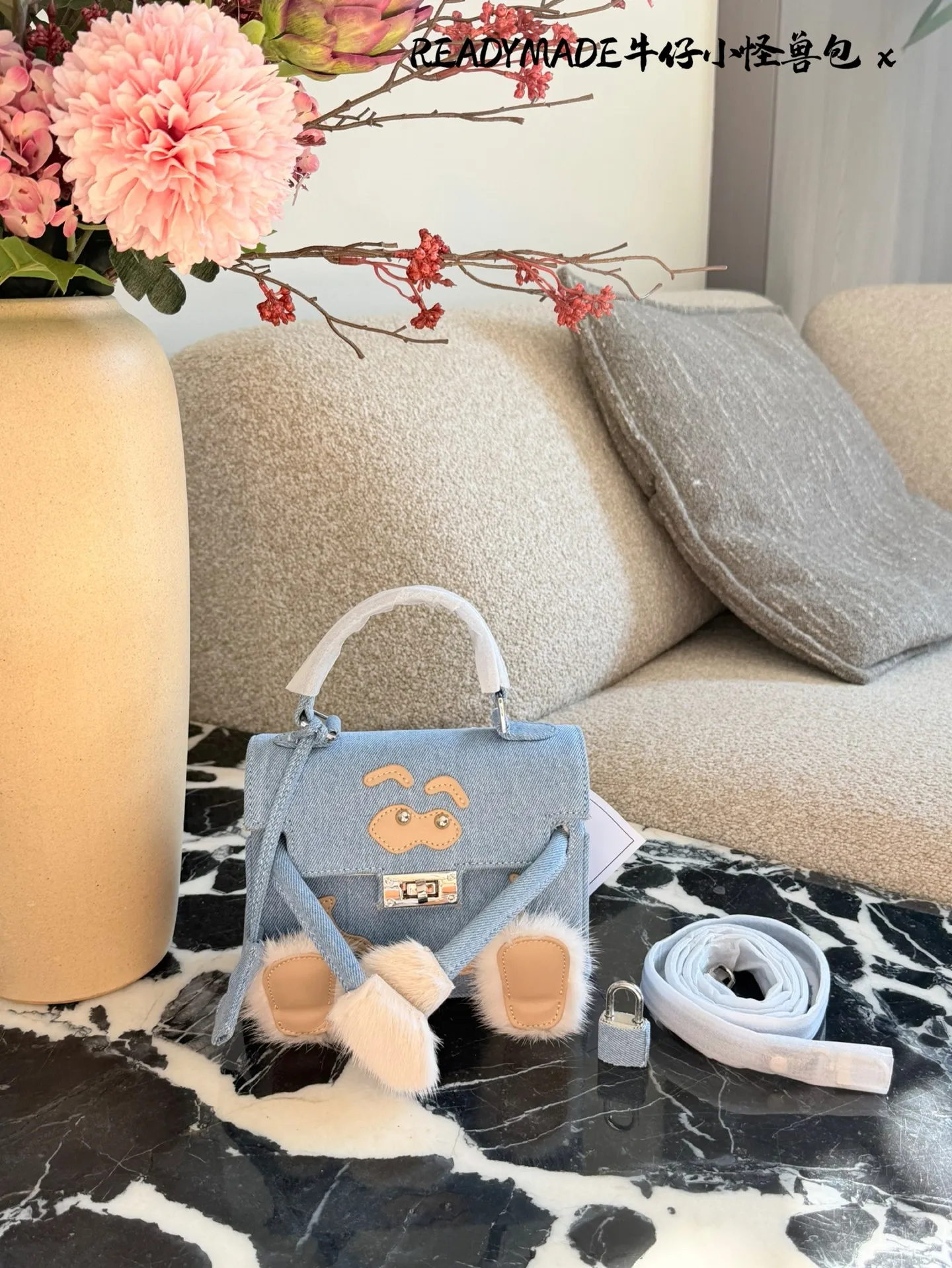 p215 READYMADE牛仔小怪兽包 国日本小众品牌READYMADE的牛仔小怪兽包，灵感来 自爱马仕Kelly Doll,浅蓝牛仔布+貂毛手脚，手感超柔软，趣味满分汁。迷你尺寸约18cm，能装手机、气垫等日常小物，手拎斜挎都OK，街头风、甜酷风都能轻松驾驭!部分配色已停产，收藏价值高，超适合喜欢个性和可爱风的姐妹们。