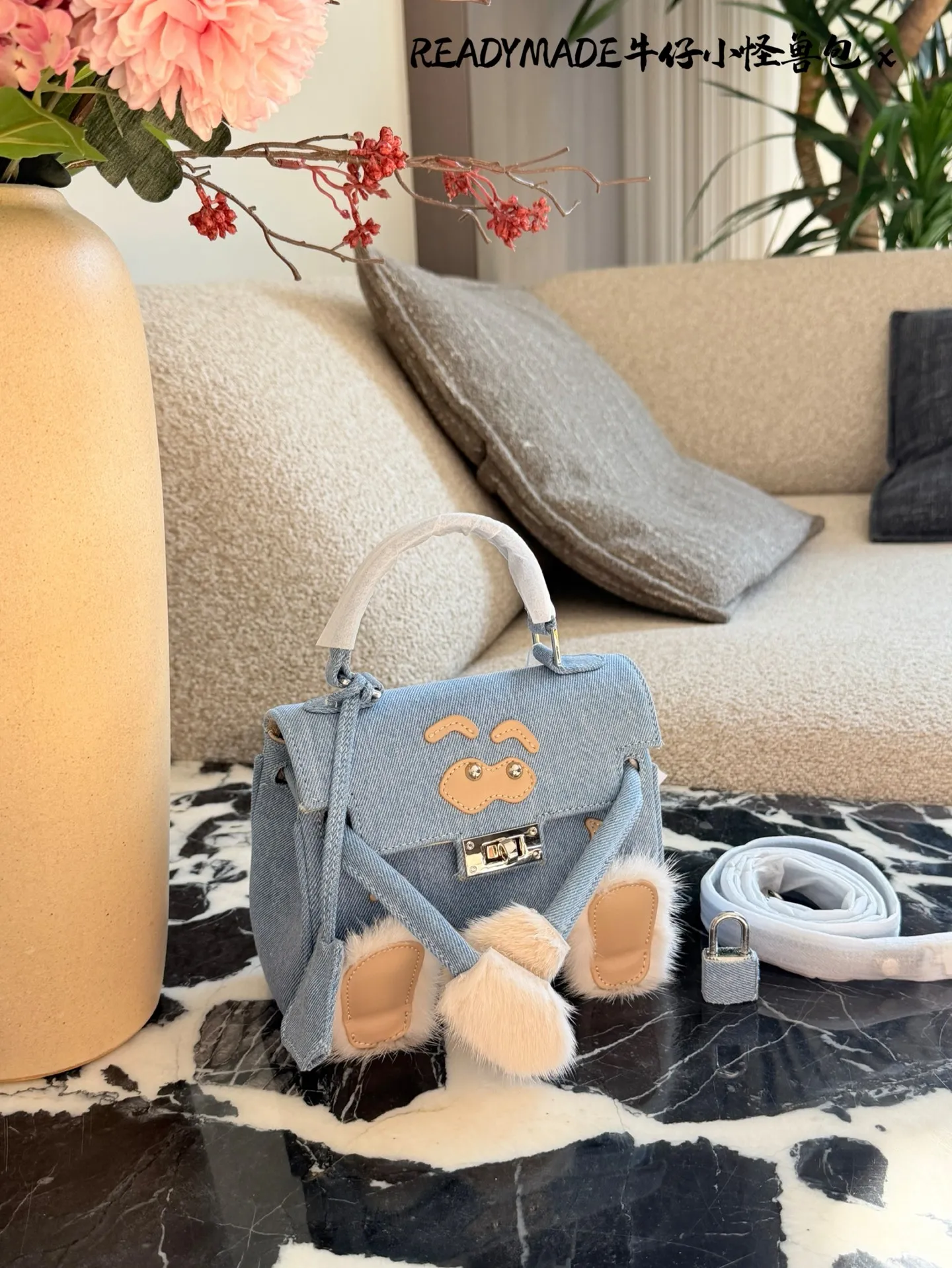 p215 READYMADE牛仔小怪兽包 国日本小众品牌READYMADE的牛仔小怪兽包，灵感来 自爱马仕Kelly Doll,浅蓝牛仔布+貂毛手脚，手感超柔软，趣味满分汁。迷你尺寸约18cm，能装手机、气垫等日常小物，手拎斜挎都OK，街头风、甜酷风都能轻松驾驭!部分配色已停产，收藏价值高，超适合喜欢个性和可爱风的姐妹们。