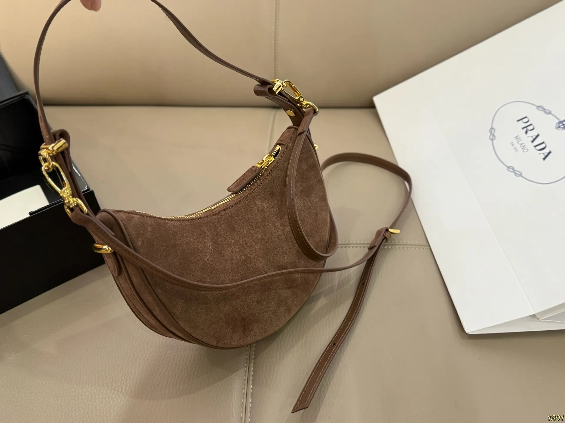 ¥180 Prada 普拉达 Araue麂皮月牙腋下包 弧形乡设计灵感源自新月,皮革+珐琅三角徽标,低调优雅又超有辨识度。双肩带设计,手提肩背都OK,容量适中,通勤休闲都能用。新月造型寓意新生与圆满,实用又时髦,是本季超火单品,明星博主都在背!搭配简约或复古穿搭,气质直接拉满尺寸23*13