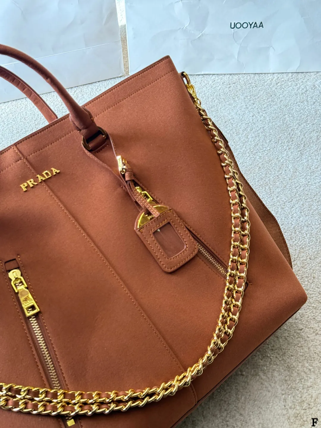 p190 Prada链条托特包 Prada这款棕色链条托特包，采用优质牛皮，手感细腻耐用。金属链条+皮革肩带，手提斜挎都OK，超百搭！正面Logo低调有辦识度，内部空间超大，通勤or短途旅行都能装下日常用品。拉链口袋设计，收纳更方便，实用又时髦，是都市女生的热门选择！ 尺寸 35 33cm