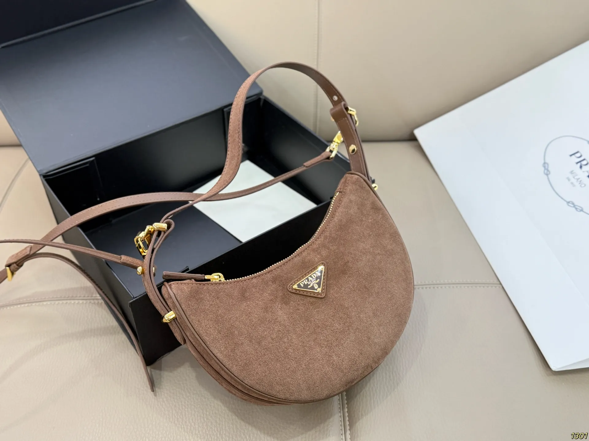 &yen;180 Prada 普拉达 Araue麂皮月牙腋下包 弧形乡设计灵感源自新月，皮革＋珐琅三角徽标，低调优雅又超有辨识度。双肩带设计，手提肩背都OK，容量适中，通勤休闲都能用。新月造型寓意新生与圆满，实用又时髦，是本季超火单品，明星博主都在背！搭配简约或复古穿搭，气质直接拉满尺寸23*13