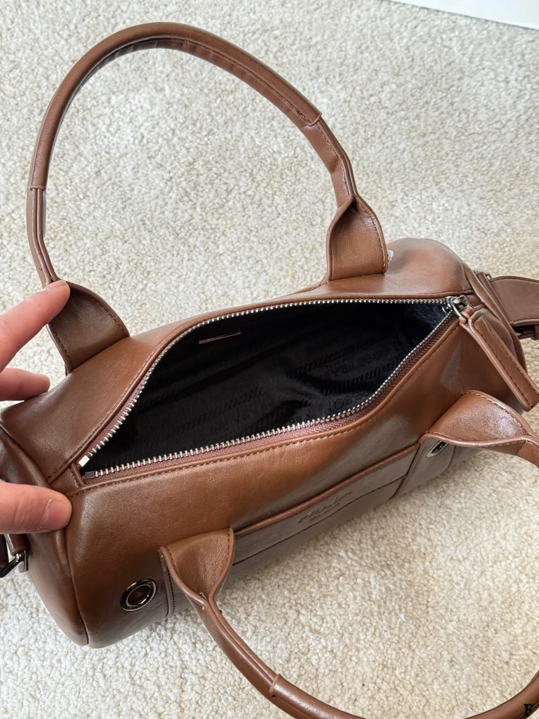 p170 Prada 26SS圆筒包 些Prada 26SS圆筒包是春夏系列新品,棕色皮革质感细腻耐用,简约复古风格超有范!圆筒造型+双提手+可拆卸肩带,手提斜挎都OK,通勤休闲都能搭。正面Logo低调有辨识度,金属环扣点缀细节满分。日本快闪首发,稀缺属性,时尚实用,Prada粉丝必入! 尺寸 30 15cm