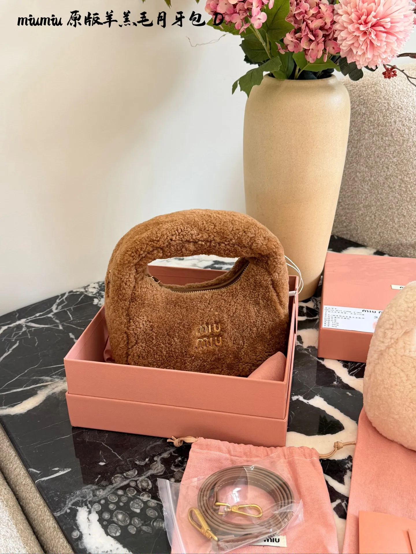 p255 Miu Miu羊羔毛Mini Wander手提包 &这款Miu Miu羊羔毛Mini Wander手提包，采用柔软羊 羔毛，触感超温暖,秋冬必备!奶茶色包身+金色L ogo刺绣，精致又有辨识度十。尺寸小巧，手提or肩背都OK,配有链条和肩带，百搭各种穿搭风格。内部空间刚好，手机、钥匙轻松收纳，实用又时髦。23cm配盒子