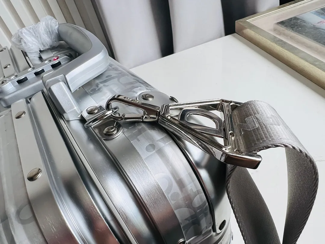 Dior联名日默瓦rimowa手提箱14寸随身登机 38cm 本季推出的 Dior & Rimowa@38 厘米手提化妆箱，可可单肩/可斜挎；选用 Damier Graphite 帆布内里，印有男装艺术总监 Virgil Abloh 设计的新款彩色交织dr系列的字母。光滑外层包裹轻巧的铝制手提和高密度斜挎带，使整个手提箱高级感倍增。箱内设计精简，左右带两居室的内测，实用且不失奢华，内里还包括 1 个拉链隔层和 1 个小插袋。 详细特征 38.0 x 16.5.0 x 22.0 cm (长 x 高 x 宽) &middot;随身上机行李尺寸 . 单肩/斜挎 ．Damier Graphite涂层定制帆布 ．两居室内衬 ．牛皮饰边 ．铝制饰件 ． ．箱内人性化合理设计 ．dr家专属内里隔层 ．顶部配有合金手柄 ．镁铝合金包角 ．内里拉链开合，配有tsa海关锁 ．4个小巧防滑底座