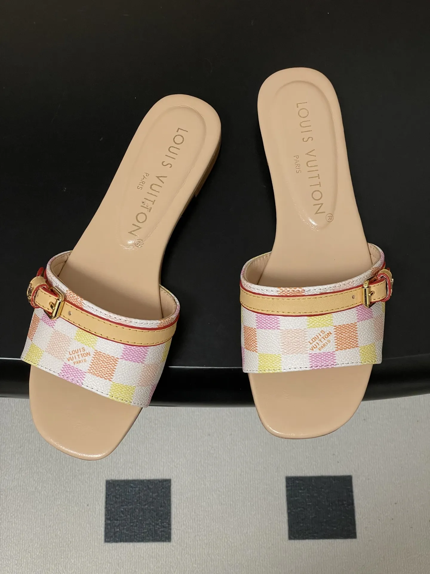 p260- 25ss夏季新款 LOUIS VUITTON 路易威登 Lv L经典棋盘格平底一字带凉拖鞋 采用经典的棋盘格图案设计，由粉色、黄色、白色等多种柔和色调组成，色彩搭配清新且富有层次感，视觉上给人活泼俏皮的感觉。同时，棋盘格作为LV的标志性元素之一，彰显品牌独特风格与辨识度。 鞋面上有一条皮质鞋带，增加了鞋子的层次感和可调节性。鞋带两端配有金属扣装饰，精致的金属配件不仅提升了鞋子的质感，还为整体造型增添了一丝时尚感和精致感。 鞋面：定制老花皮 内里垫脚：羊皮 鞋底：意大利加厚真皮大底 码数：35-41（40.41定做不退换）