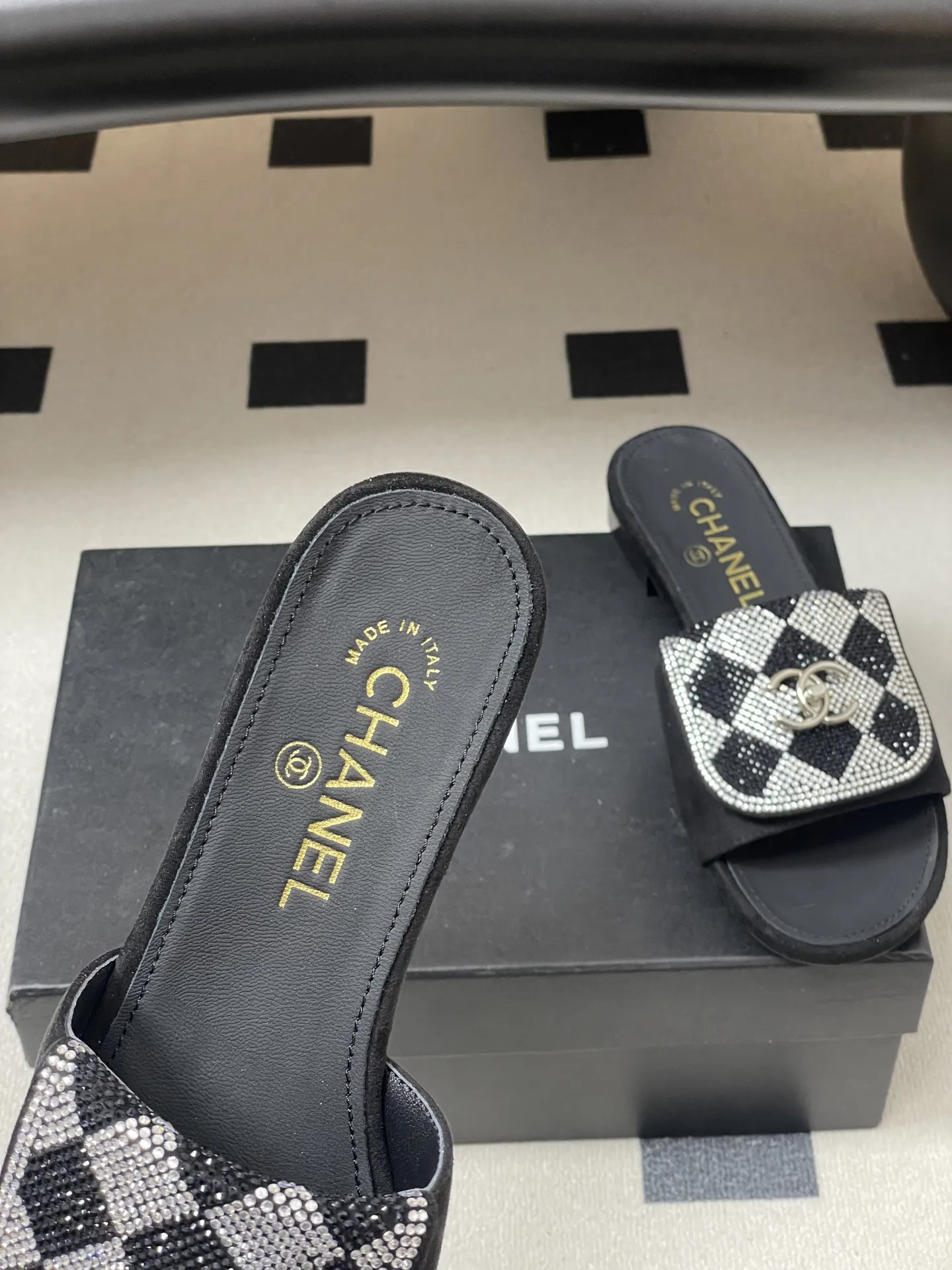 p240- 26Fw春夏新款Chanel小香经典翻盖书包扣水钻一字拖鞋新颖烫钻棋盘格粗跟拖鞋 经典永不过时 简约大气，标志性翻盖双C书包扣设计～手工镶嵌的水钻棋盘轮廓成星河，抬脚时折射出香槟色光晕，显瘦百搭～脚感非常舒适！凸显优雅的爆品 小香粉必入！ 鞋面：羊猄皮/烫钻 内里垫脚：羊皮 高跟：平底/粗跟5cm 鞋底：意大利真皮大底 码数：35-39（40.41.42定做不退换）