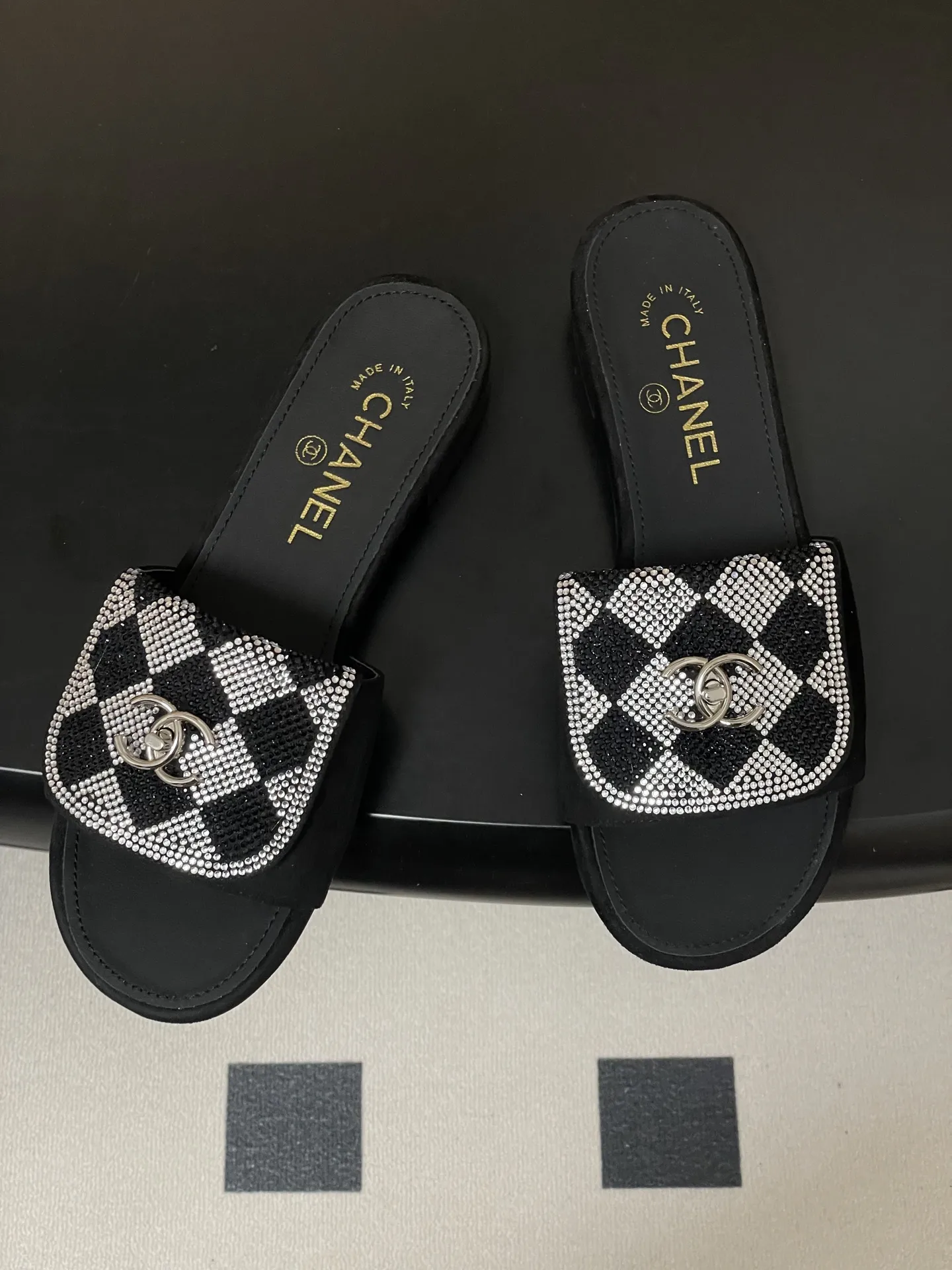 p240- 26Fw春夏新款Chanel小香经典翻盖书包扣水钻一字拖鞋新颖烫钻棋盘格粗跟拖鞋 经典永不过时 简约大气，标志性翻盖双C书包扣设计～手工镶嵌的水钻棋盘轮廓成星河，抬脚时折射出香槟色光晕，显瘦百搭～脚感非常舒适！凸显优雅的爆品 小香粉必入！ 鞋面：羊猄皮/烫钻 内里垫脚：羊皮 高跟：平底/粗跟5cm 鞋底：意大利真皮大底 码数：35-39（40.41.42定做不退换）