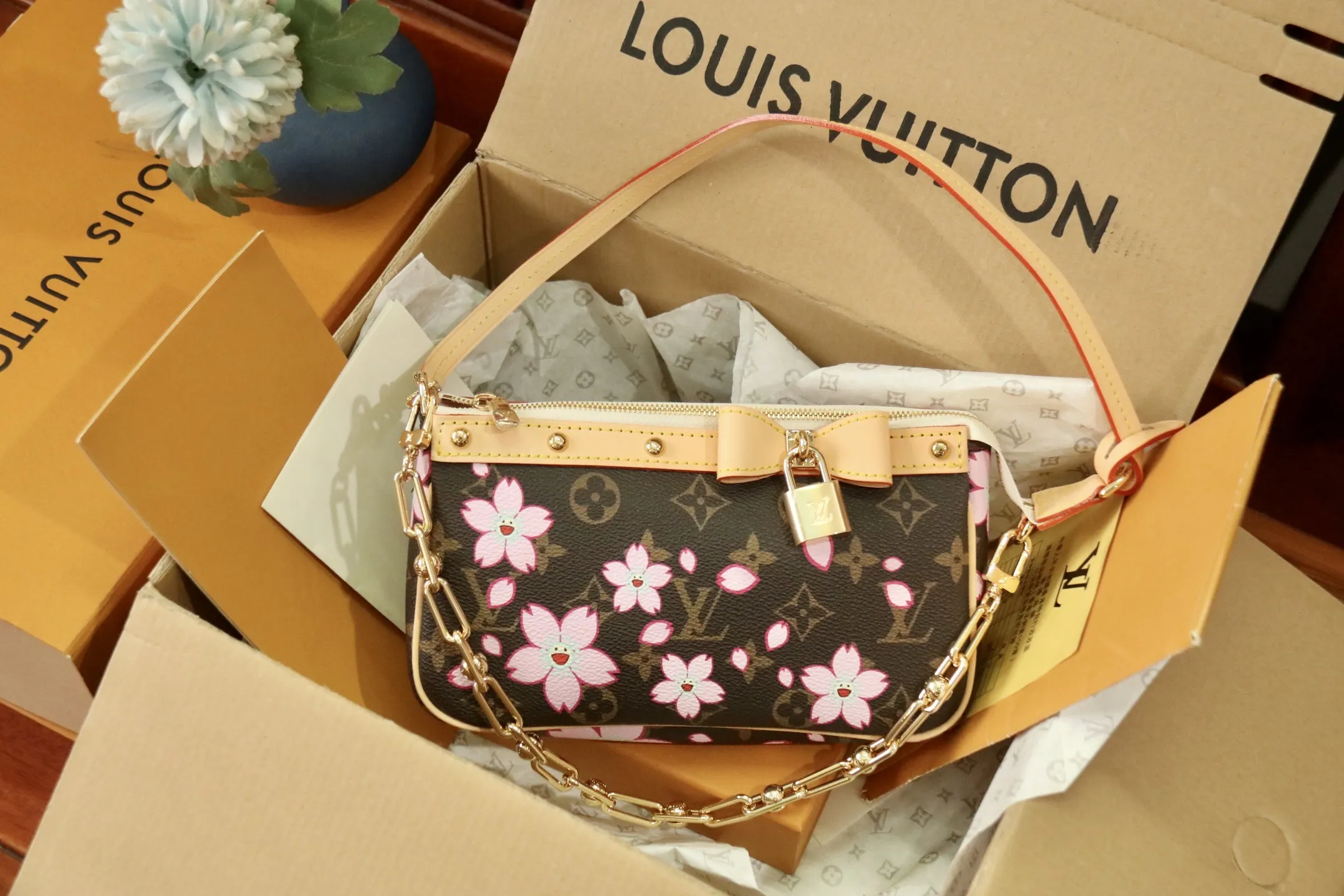 M13666樱花 🌟P350 本款 Pochette Accessoires 手袋为经典 Monogram 帆布融入村上隆笔下的明媚 Cherry Blossom 图案，以玩趣格调道出路易威登 x 村上隆复刻系列的鲜明元素。皮革蝴蝶结与 LV 铭纹挂锁点亮上缘，耀目饰钉与可拆卸链条注入一丝不羁气息。13 x 4 x 22 厘米
