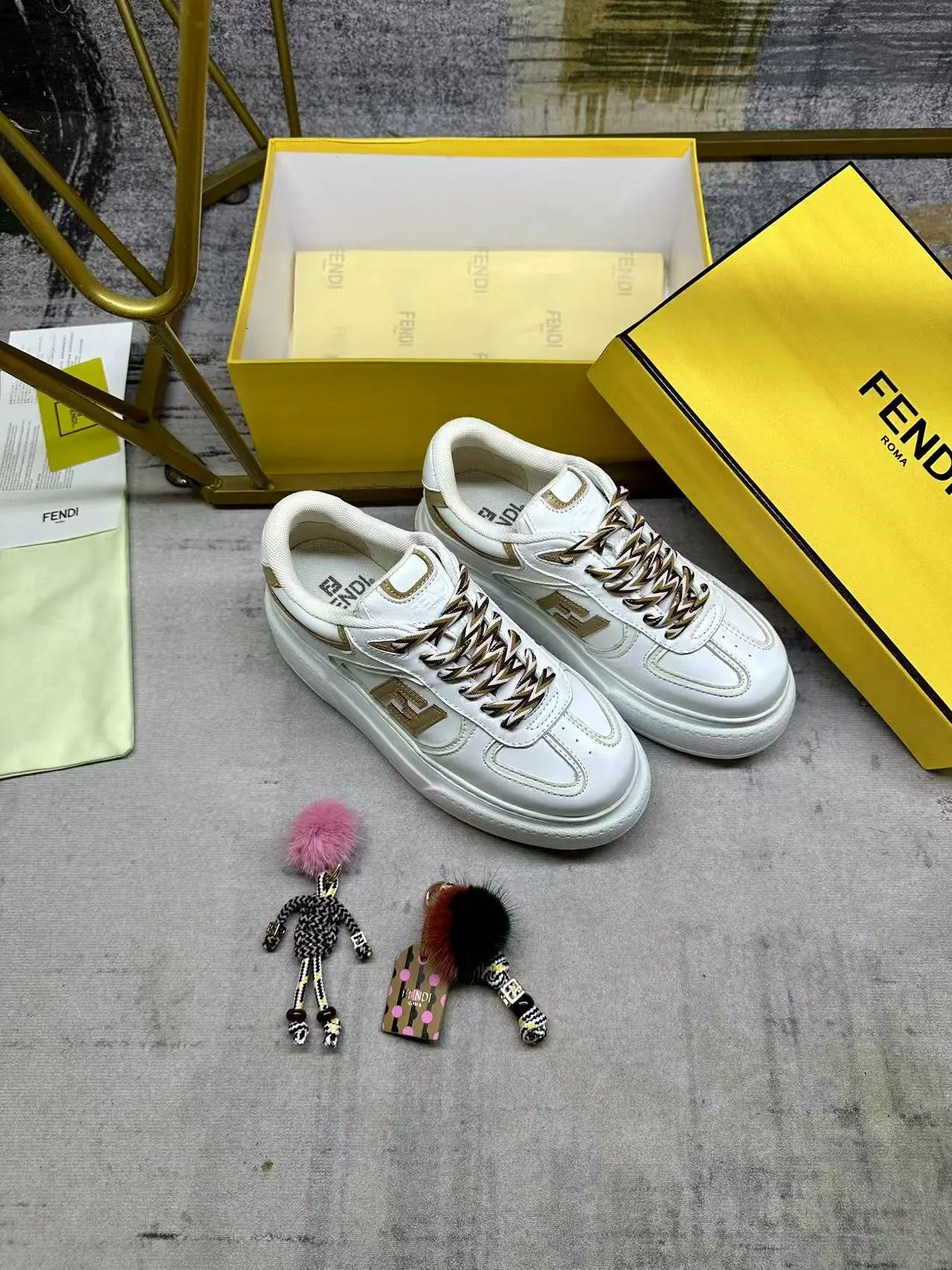 FENDI Match系带运动鞋。白色面料,带米色细节。侧边饰有撞色皮革FF贴花,白色、米色和棕色登山鞋带。橡胶厚鞋底,后跟处饰有超大凸纹压花FENDI字样。鞋舌上饰有金属环挂饰:右鞋上饰有带撞色貂毛细节和金色金属FF图案手链的编绳小玩偶。左鞋上饰有一条带撞色貂毛双绒球的编绳,饰有金属FF圆珠以及Pequin印花图案和标志(玩偶可拆卸),35-42码,P305