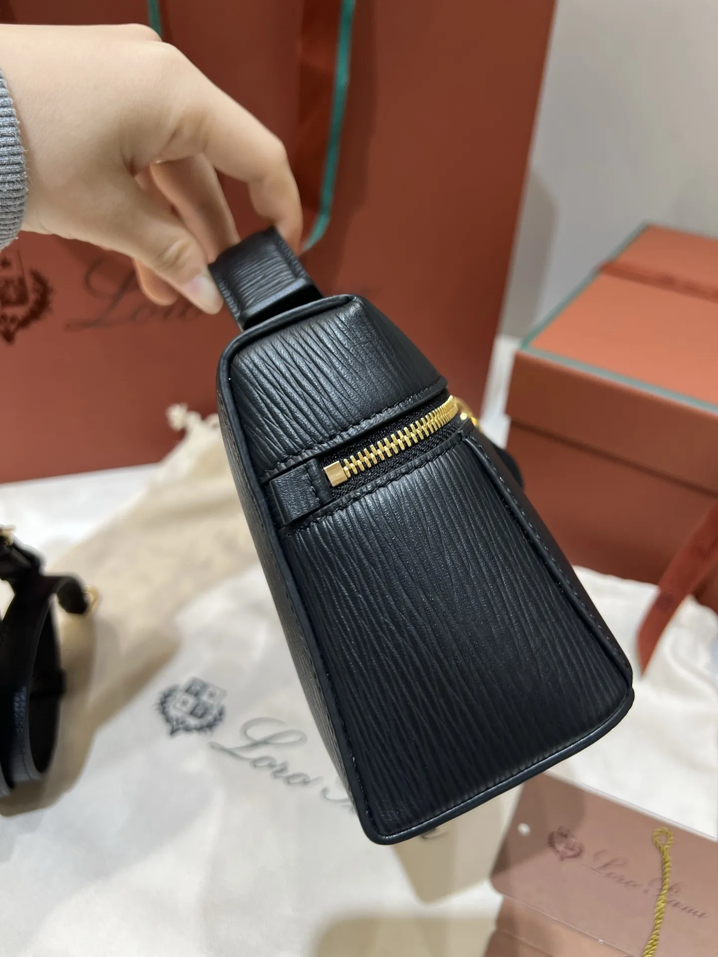 💰600 Extra Bag23手袋【水波纹黑色】 采用Saddle Leather牛皮革材质精心制作,饰以繁复精致的明迹缝线,既可手提,亦可斜挎。双拉链开合处悬挂着LoroPiana的标志性挂饰,并搭配精致的皮革钥匙扣,可拆卸可调节肩带 双向拉链开合,饰有挂饰 内部皮革卡槽 皮革钥匙扣 绒面革衬里 金属色配件尺寸:23x12x 厘米手柄高度:5厘米 肩带长度:46-58厘米