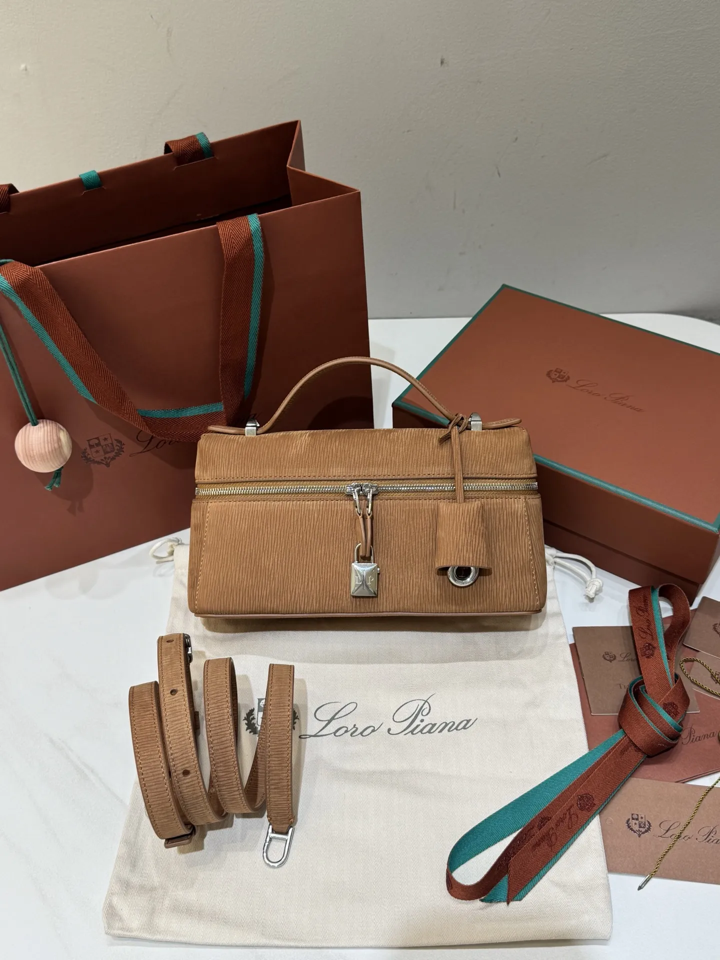 💰600 Extra Bag23手袋【天鹅绒水波纹暖棕褐色】 采用Saddle Leather牛皮革材质精心制作,饰以繁复精致的明迹缝线,既可手提,亦可斜挎。双拉链开合处悬挂着LoroPiana的标志性挂饰,并搭配精致的皮革钥匙扣,可拆卸可调节肩带 双向拉链开合,饰有挂饰 内部皮革卡槽 皮革钥匙扣 绒面革衬里 金属色配件尺寸:23x12x 厘米手柄高度:5厘米 肩带长度:46-58厘米