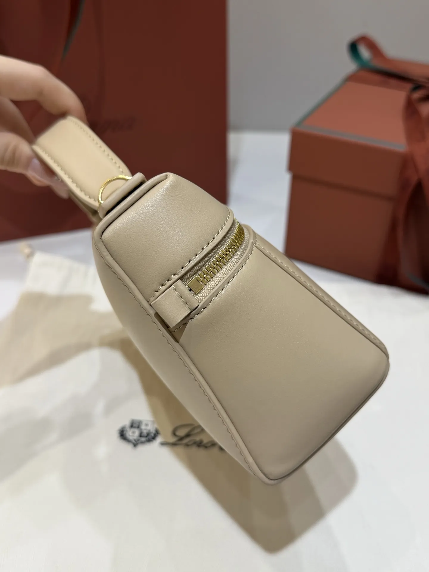 💰600 Extra Bag23手袋【平纹浅乳香】 采用Saddle Leather牛皮革材质精心制作，饰以繁复精致的明迹缝线，既可手提，亦可斜挎。双拉链开合处悬挂着LoroPiana的标志性挂饰，并搭配精致的皮革钥匙扣，可拆卸可调节肩带 双向拉链开合，饰有挂饰 内部皮革卡槽 皮革钥匙扣 绒面革衬里 金属色配件尺寸：23x12x 厘米手柄高度：5厘米 肩带长度：46-58厘米