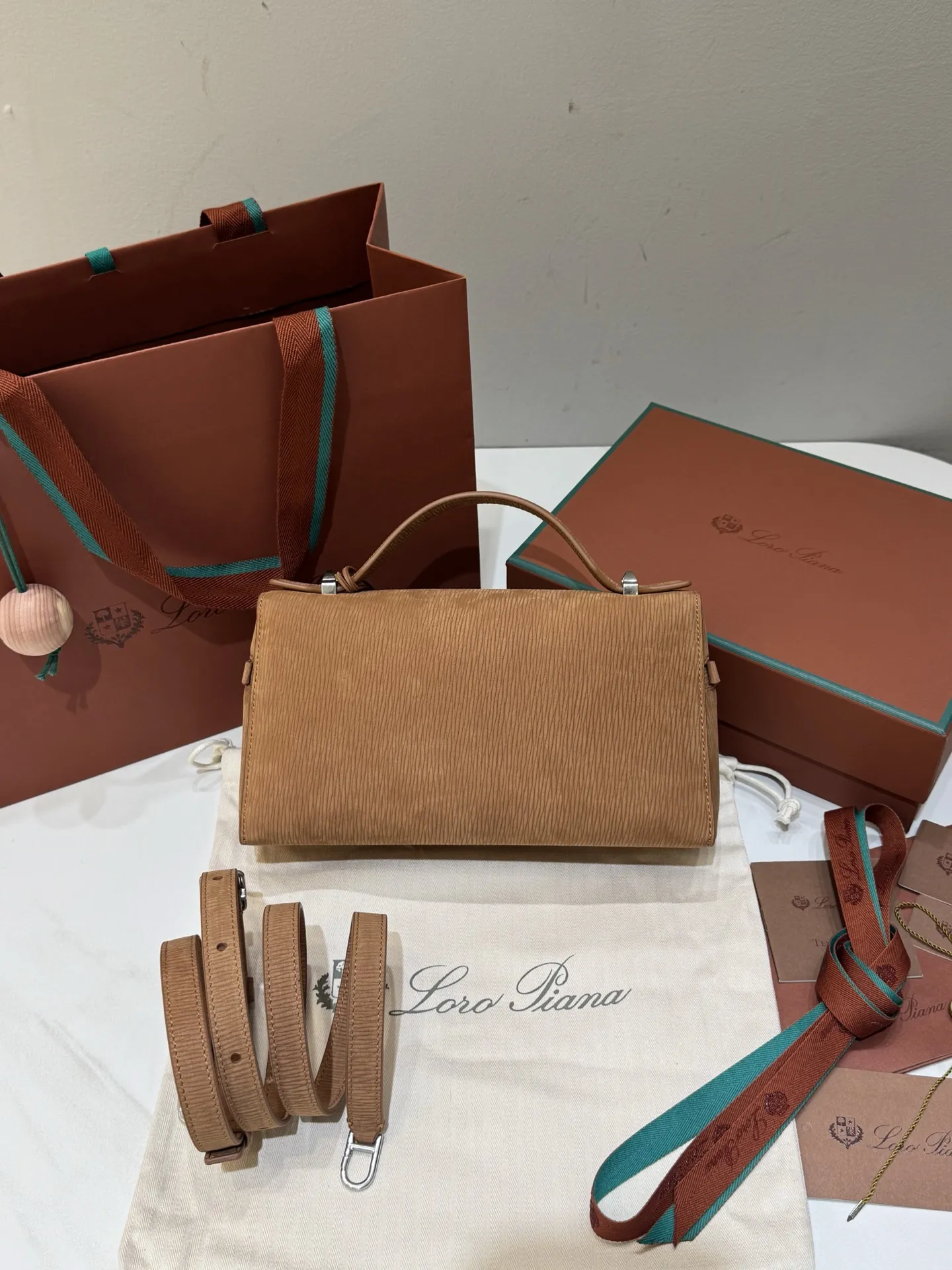 💰600 Extra Bag23手袋【天鹅绒水波纹暖棕褐色】 采用Saddle Leather牛皮革材质精心制作，饰以繁复精致的明迹缝线，既可手提，亦可斜挎。双拉链开合处悬挂着LoroPiana的标志性挂饰，并搭配精致的皮革钥匙扣，可拆卸可调节肩带 双向拉链开合，饰有挂饰 内部皮革卡槽 皮革钥匙扣 绒面革衬里 金属色配件尺寸：23x12x 厘米手柄高度：5厘米 肩带长度：46-58厘米