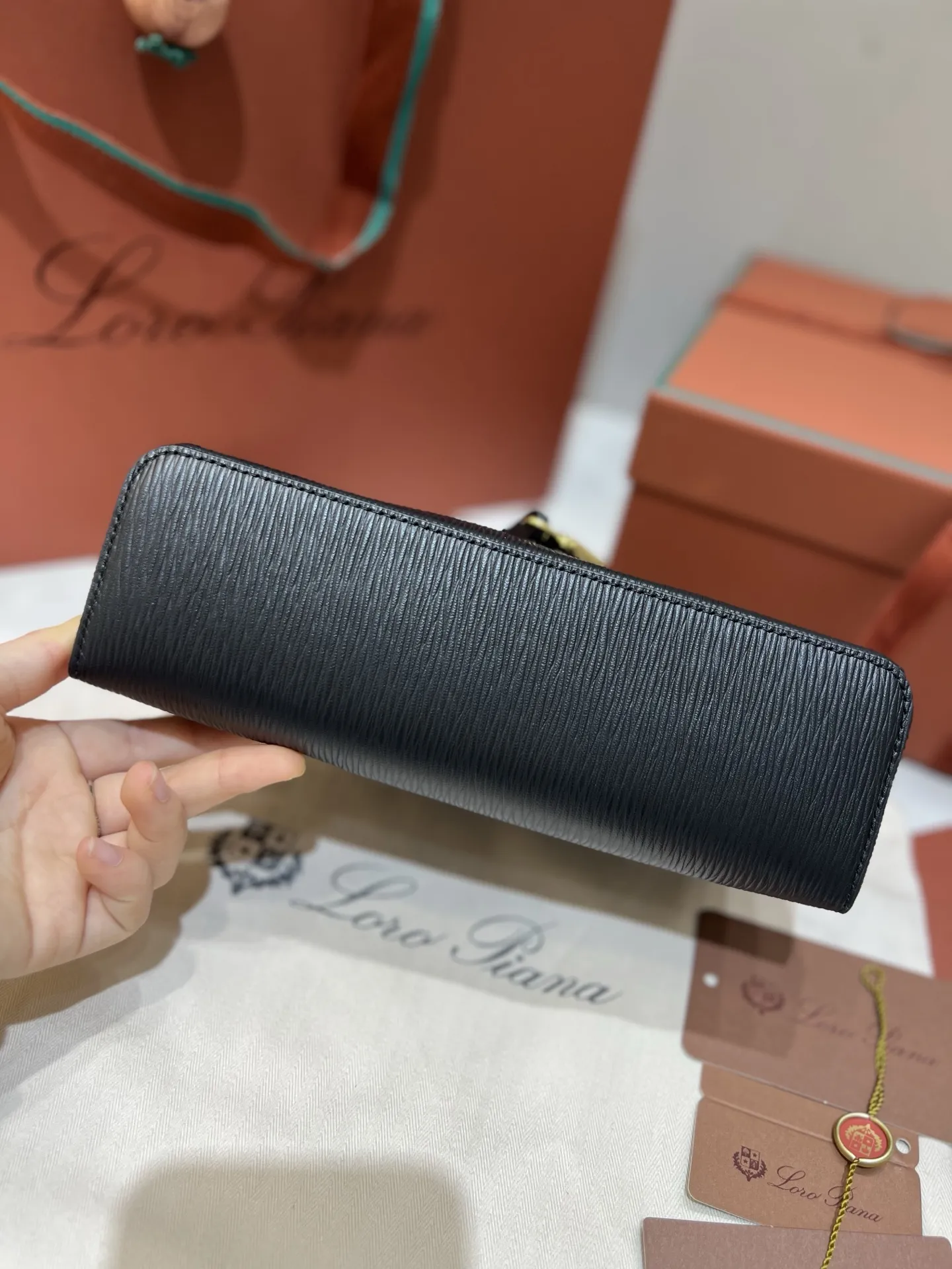 💰600 Extra Bag23手袋【水波纹黑色】 采用Saddle Leather牛皮革材质精心制作，饰以繁复精致的明迹缝线，既可手提，亦可斜挎。双拉链开合处悬挂着LoroPiana的标志性挂饰，并搭配精致的皮革钥匙扣，可拆卸可调节肩带 双向拉链开合，饰有挂饰 内部皮革卡槽 皮革钥匙扣 绒面革衬里 金属色配件尺寸：23x12x 厘米手柄高度：5厘米 肩带长度：46-58厘米