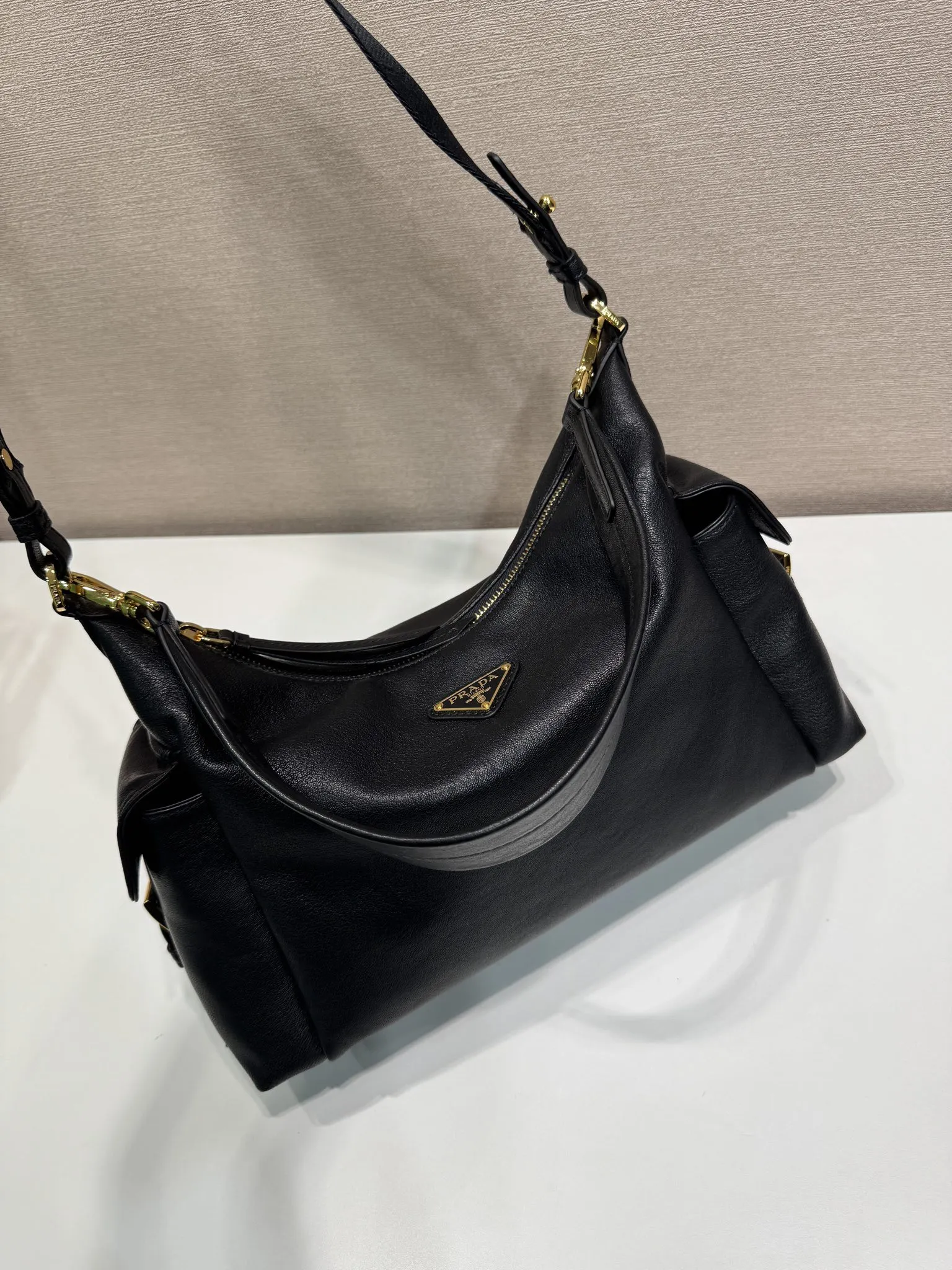 Prada 1:1 premium soft grained leather hobo bag in black with triangle logo and dual shoulder straps on display stand - xiashuluxe