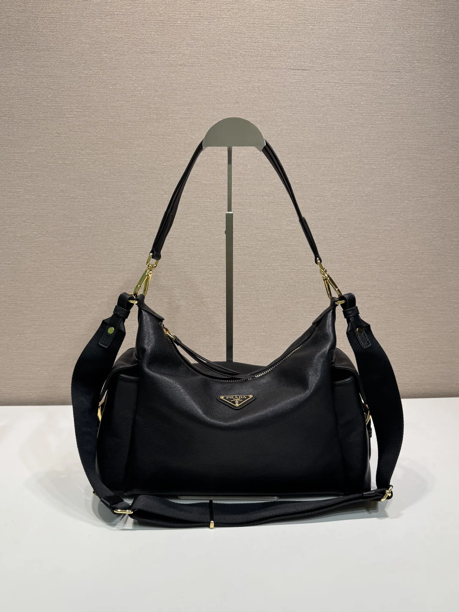 Prada 1:1 premium soft grained leather hobo bag in black with triangle logo and dual shoulder straps on display stand - xiashuluxe
