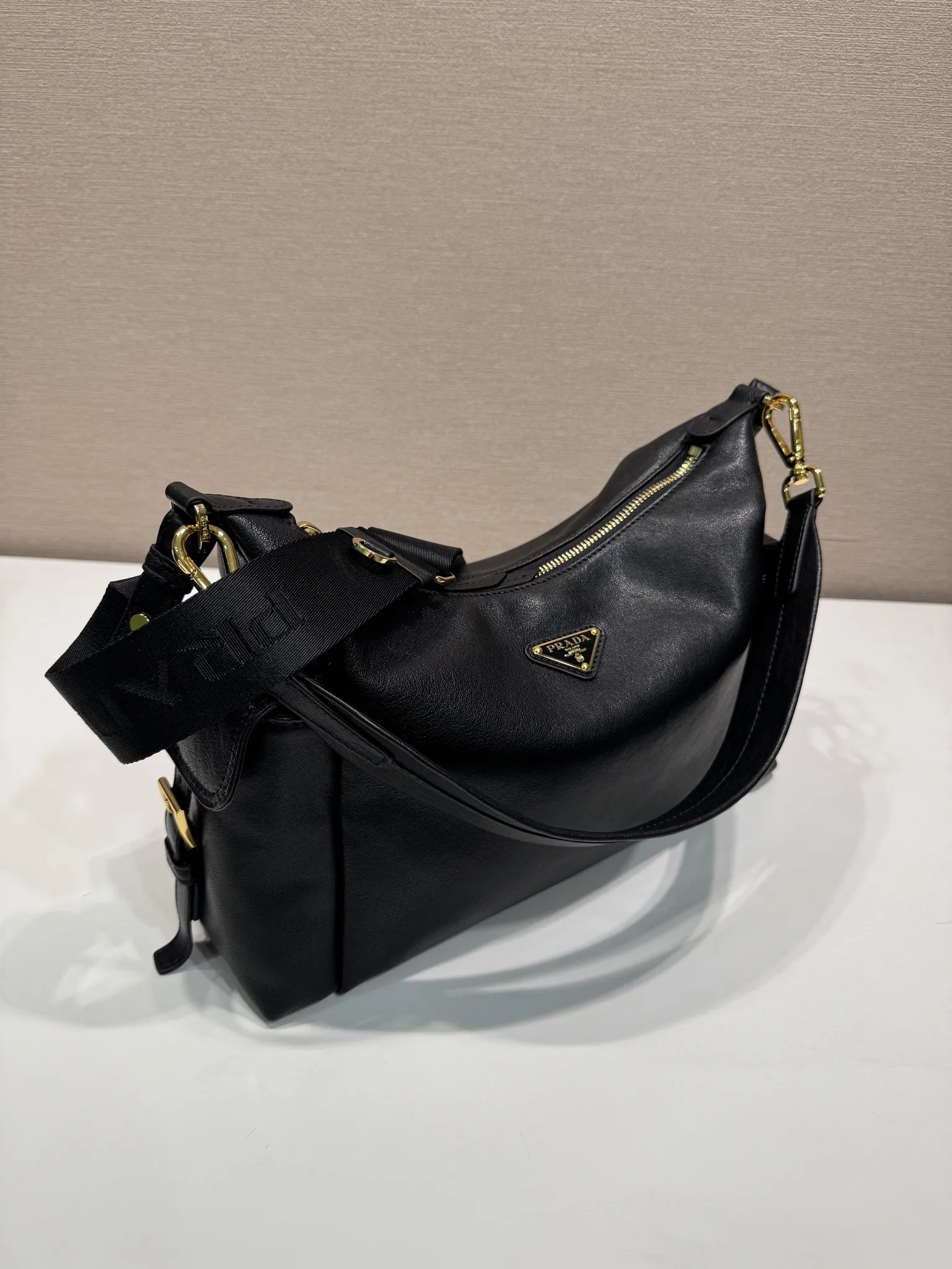 Prada 1:1 premium soft grained leather hobo bag in black with triangle logo and dual shoulder straps on display stand - xiashuluxe