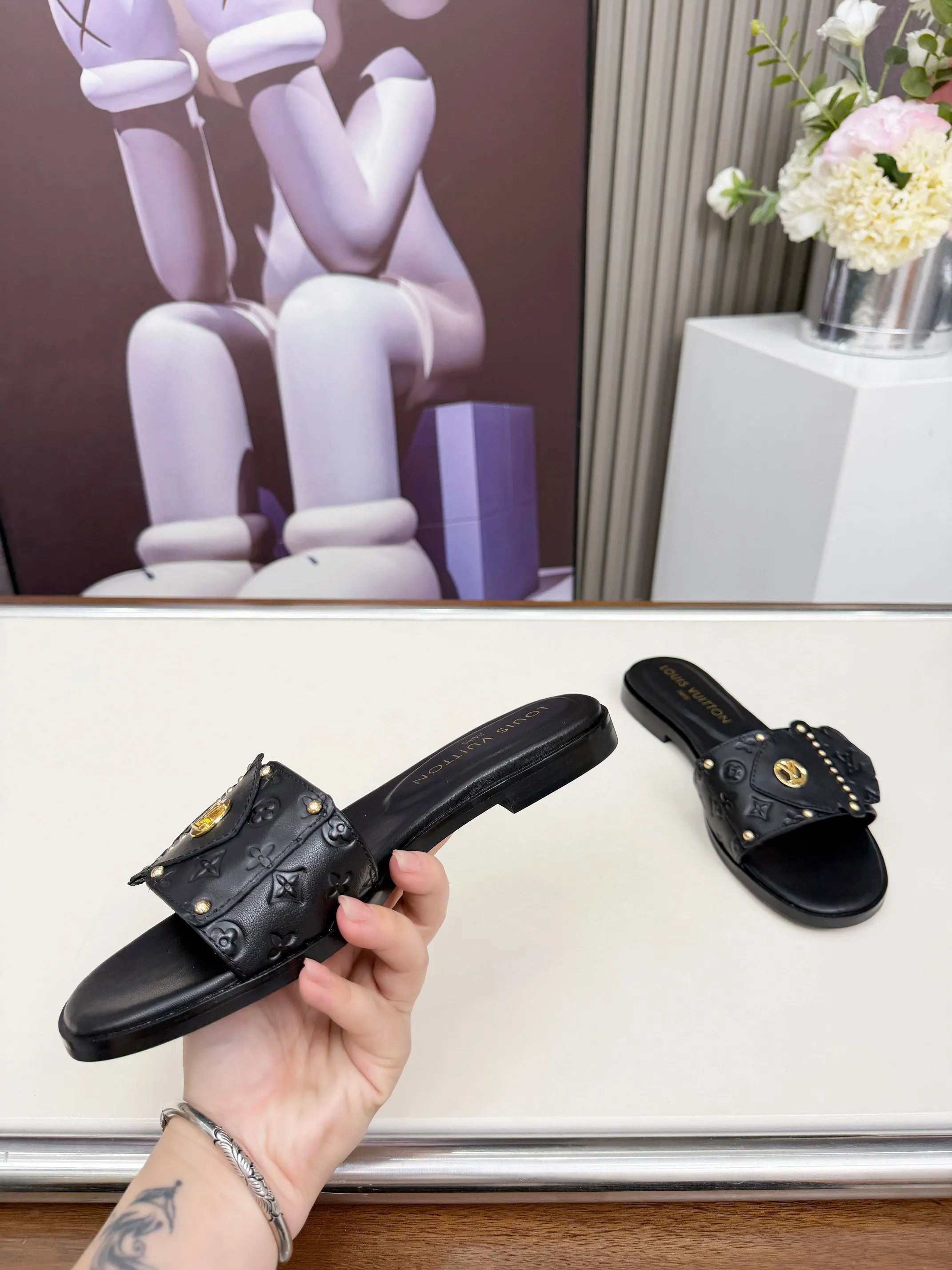 LV 1:1 premium Revival flat mules in black and white embossed Monogram leather with gold-tone studs and lock detail on display - xiashuluxe
