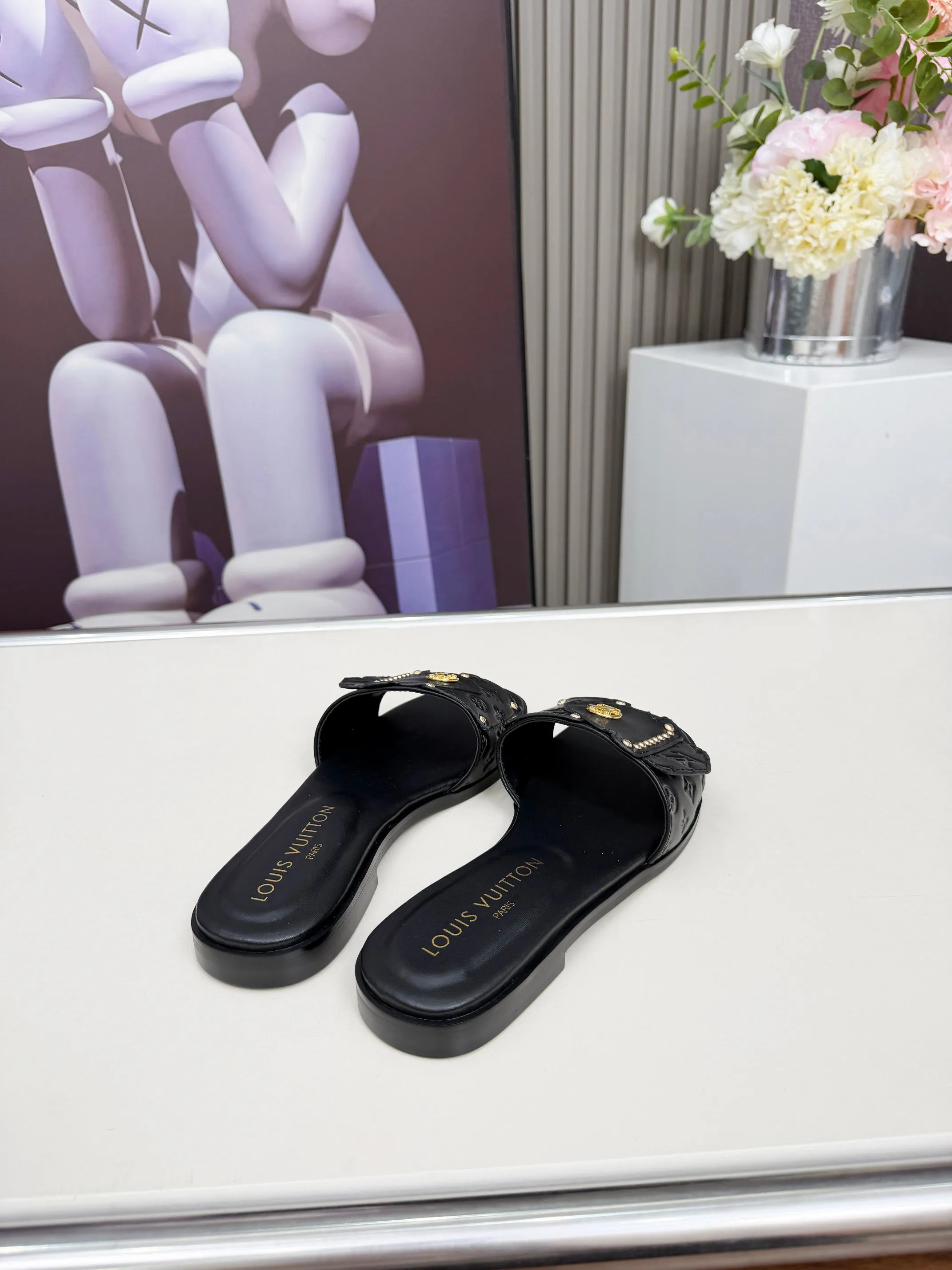 LV 1:1 premium Revival flat mules in black and white embossed Monogram leather with gold-tone studs and lock detail on display - xiashuluxe