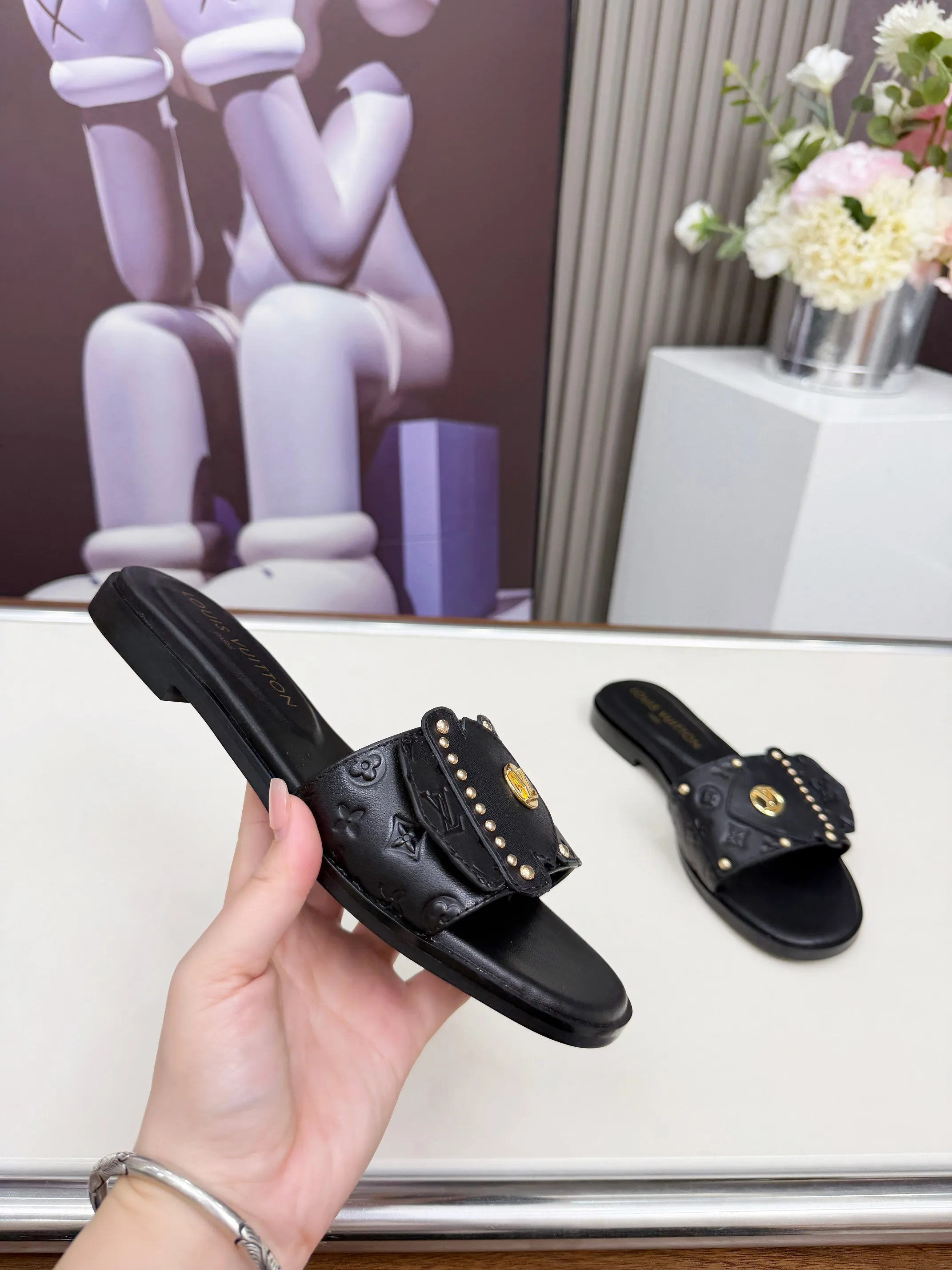 LV 1:1 premium Revival flat mules in black and white embossed Monogram leather with gold-tone studs and lock detail on display - xiashuluxe