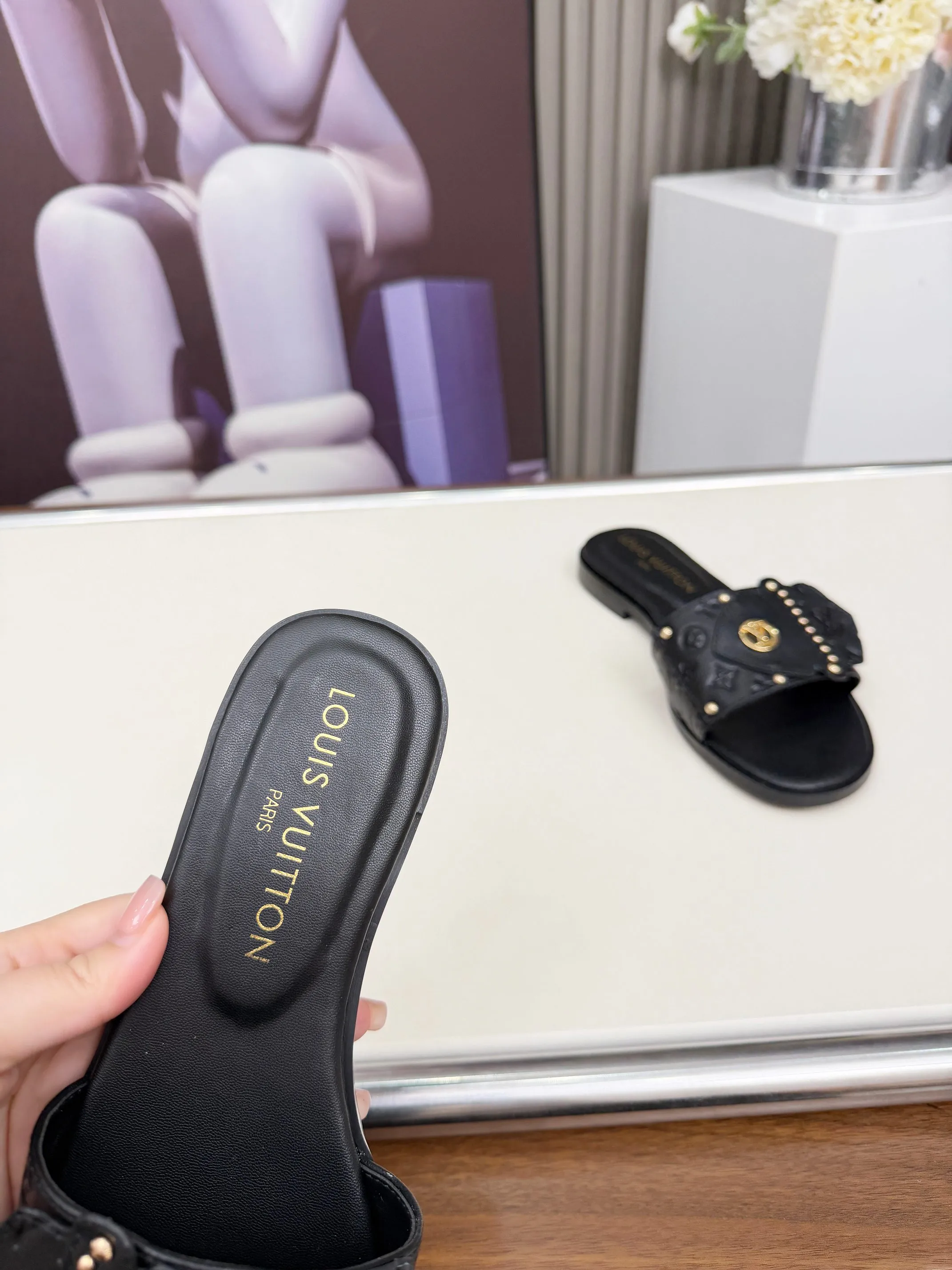 LV 1:1 premium Revival flat mules in black and white embossed Monogram leather with gold-tone studs and lock detail on display - xiashuluxe