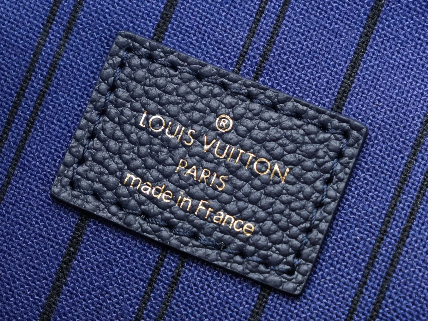 Front view of two Louis Vuitton Pochette Métis bags in Monogram Empreinte leather: one dark burgundy (Bordeaux) and one dark navy blue, placed on a white shelf with S-lock hardware, a partial Monogram bag and orange gift box background.