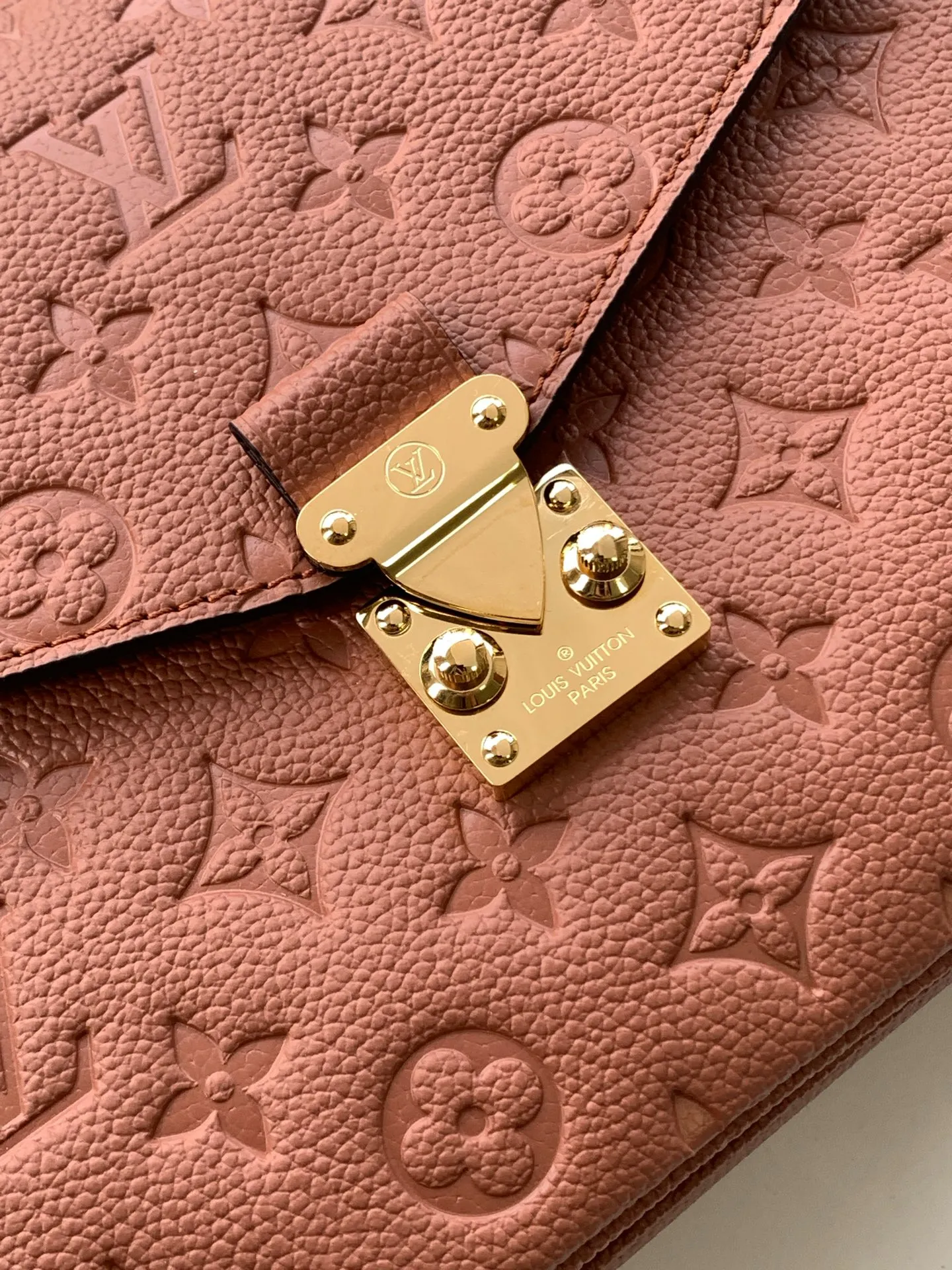 Close-up of polished solid brass S-lock clasp with crisp LV engraving on brown leather bag