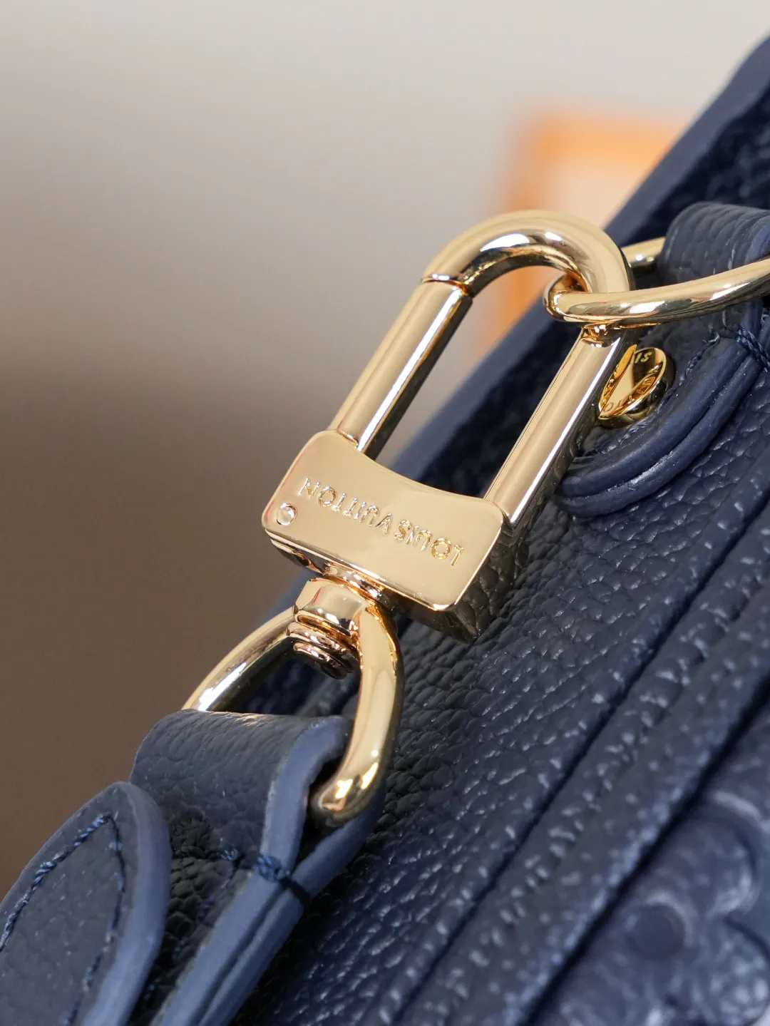 Front view of two Louis Vuitton Pochette M&eacute;tis bags in Monogram Empreinte leather: one dark burgundy (Bordeaux) and one dark navy blue, placed on a white shelf with S-lock hardware, a partial Monogram bag and orange gift box background.