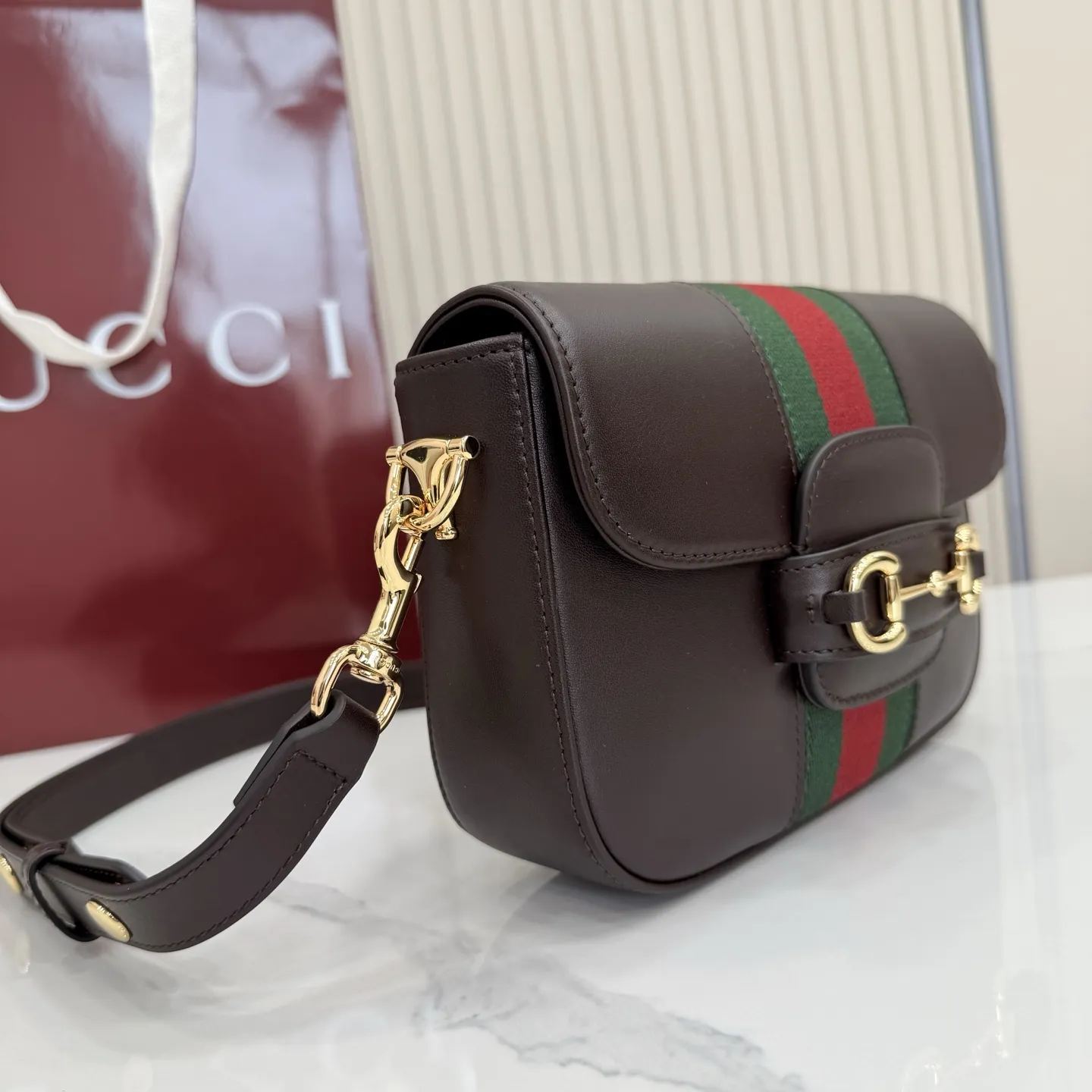 p660。【配全套专柜包装】‼️2026春夏系列全新上市。Gucci Horsebit 1955 系列包袋呈现柔韧雅致的廓形。此款式甄选柔软牛皮革打造,饰有Web织带细节,另配一条简约的可调节牛皮革肩带。 深棕色软皮 金色调配件 米色帆布衬里饰钻石菱格纹图案 马衔扣和织带 可拆卸和可调节牛皮革肩带,配搭扣,高:30厘米 翻盖开合 型号:866762。 尺寸:21厘米(宽)x 14.5厘米(高)x 5.5厘米(深) 重量:约0.5千克 颜色:深棕色/全皮。 意大利创作