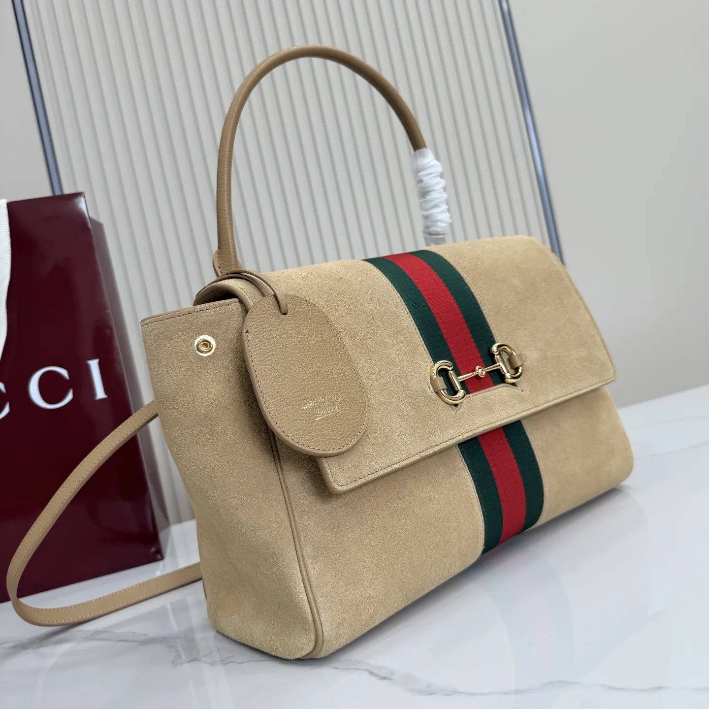 p710。【配全套包装】‼️Generation Gucci古驰世代系列深入探索品牌的典藏元素,将不同世代的设计融合为统一的美学叙事。这款款式以手提包设计向品牌标志性的马衔扣元素致敬,柔软的绒面皮革呈现精致的配色。 沙色柔软绒面材质 沙色皮革滚边 金色调配件 沙色帆布衬里,饰Diamante图案 马衔扣、织带和皮革标牌,带有“Made in Italy Gucci”标志 饰按扣 内部:1个拉链口袋,1个开口口袋 手柄垂直高度:17厘米 可拆卸和可调节皮革肩带下垂长度:42 - 54厘米;长度:93 - 112厘米 磁扣开合 型号:875018。 尺寸:30厘米(宽)x 21厘米(高)x 12厘米(深) 重量:约685克 颜色:杏色/绒皮。 意大利创作