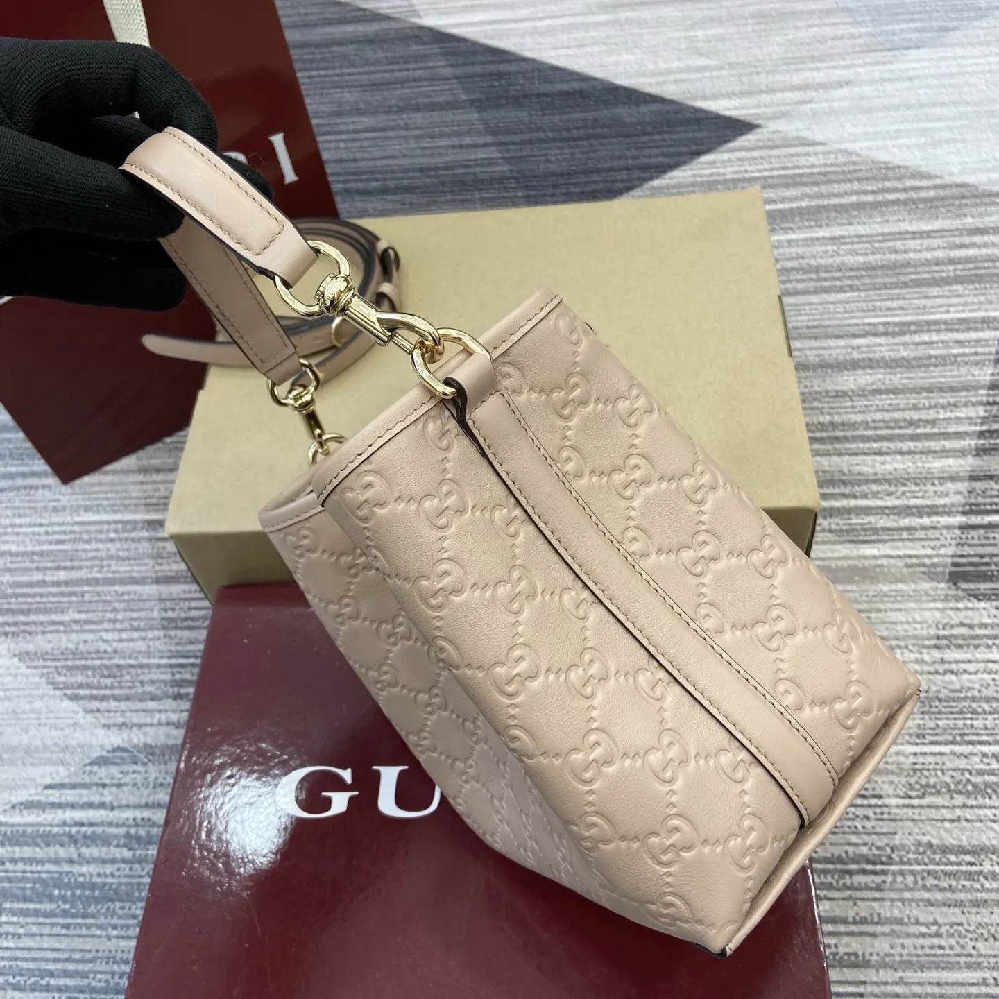 p570。【配全套专柜包装】‼️GG Emblem系列焕新诠释品牌的隽永优雅风范和精湛工艺。这款水桶包采用织带棉质衬里，设有一个内部隔层，实用性出众。 杏粉色GG印花压纹牛皮革 浅金色调配件 灰褐色棉麻衬里 另配有用于系挂可拆卸物品的D形环 内部：两个隔层和一个中央按扣隔层 钩扣开合顶部手柄（高度：14厘米） 可拆卸可调节牛皮革肩带（高度：52厘米 - 57.5厘米；长度：107厘米 - 114厘米） 磁力按扣开合 型号：815118。 尺寸：19厘米（宽）x 18厘米（高）x 11厘米（深） 重量：约0.45千克 颜色：杏粉色/压花。 意大利创作