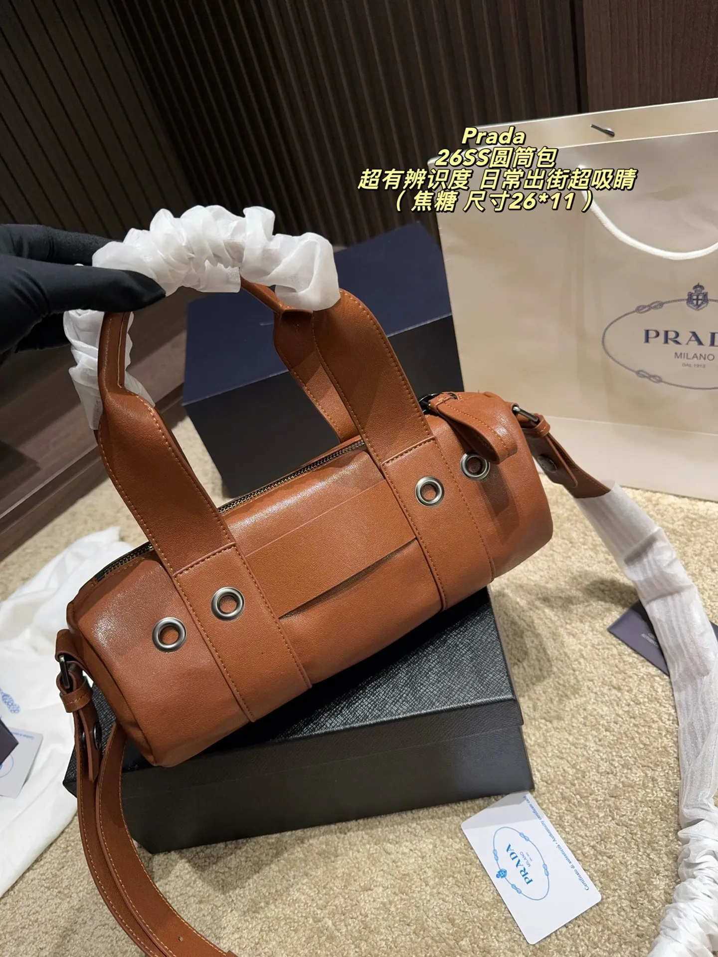 p180配盒⚠️尺寸26*11 普拉达Prada 26SS圆筒包是2023春夏系列快闪限定，棕色皮革+金属孔眼，简约又有工业感✨。圆筒造型容量适中，通勤休闲都OK！肩带可调节，手提斜挎随心切换，实用性满分。无性别设计，男女都能轻松驾驭，时尚又百搭，超适合喜欢个性风格的你！