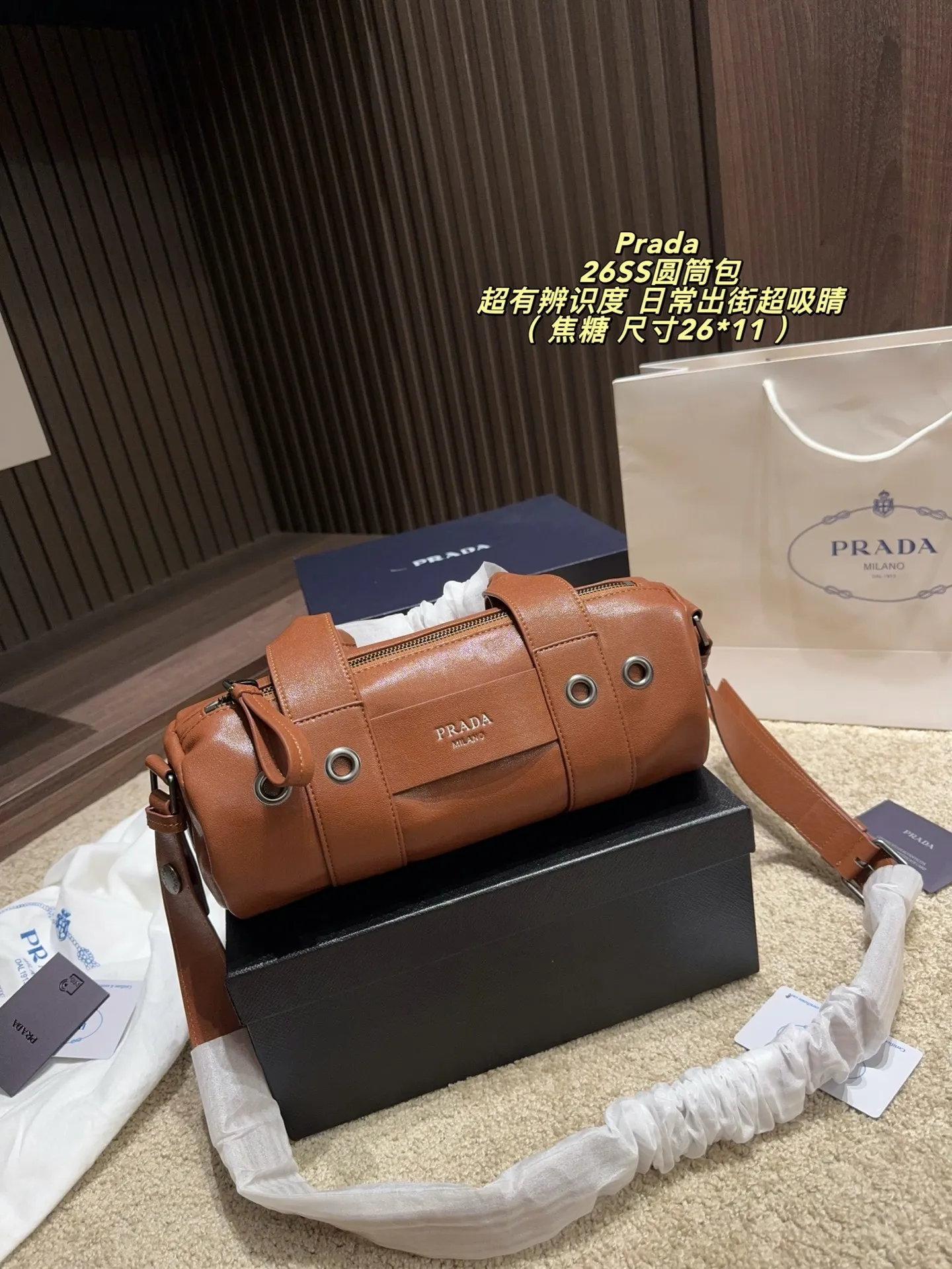 p180配盒⚠️尺寸26*11 普拉达Prada 26SS圆筒包是2023春夏系列快闪限定，棕色皮革+金属孔眼，简约又有工业感✨。圆筒造型容量适中，通勤休闲都OK！肩带可调节，手提斜挎随心切换，实用性满分。无性别设计，男女都能轻松驾驭，时尚又百搭，超适合喜欢个性风格的你！