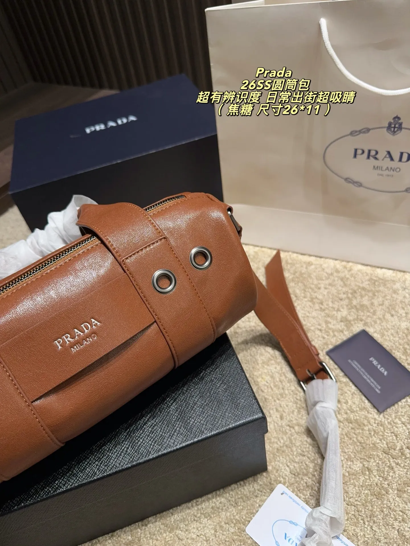 p180配盒⚠️尺寸26*11 普拉达Prada 26SS圆筒包是2023春夏系列快闪限定，棕色皮革+金属孔眼，简约又有工业感✨。圆筒造型容量适中，通勤休闲都OK！肩带可调节，手提斜挎随心切换，实用性满分。无性别设计，男女都能轻松驾驭，时尚又百搭，超适合喜欢个性风格的你！