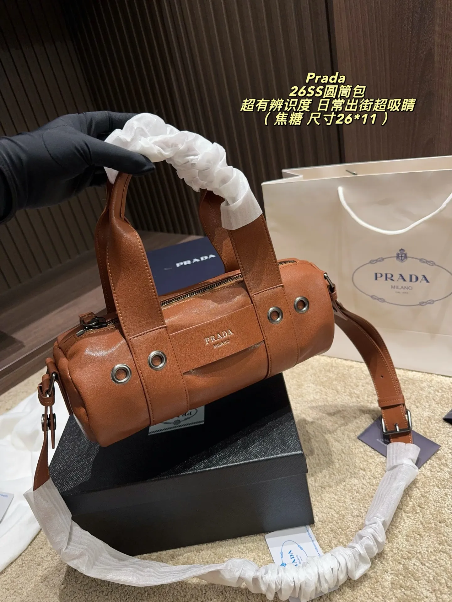p180配盒⚠️尺寸26*11 普拉达Prada 26SS圆筒包是2023春夏系列快闪限定，棕色皮革+金属孔眼，简约又有工业感✨。圆筒造型容量适中，通勤休闲都OK！肩带可调节，手提斜挎随心切换，实用性满分。无性别设计，男女都能轻松驾驭，时尚又百搭，超适合喜欢个性风格的你！