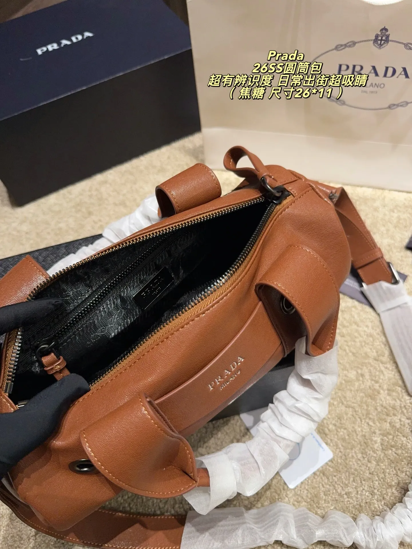 p180配盒⚠️尺寸26*11 普拉达Prada 26SS圆筒包是2023春夏系列快闪限定，棕色皮革+金属孔眼，简约又有工业感✨。圆筒造型容量适中，通勤休闲都OK！肩带可调节，手提斜挎随心切换，实用性满分。无性别设计，男女都能轻松驾驭，时尚又百搭，超适合喜欢个性风格的你！