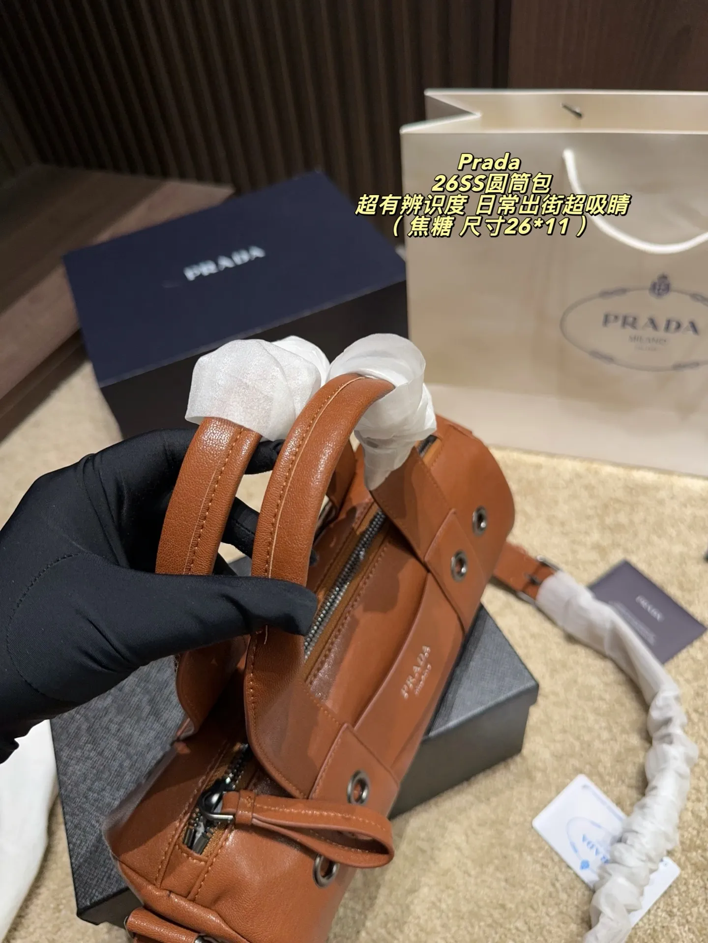 p180配盒⚠️尺寸26*11 普拉达Prada 26SS圆筒包是2023春夏系列快闪限定，棕色皮革+金属孔眼，简约又有工业感✨。圆筒造型容量适中，通勤休闲都OK！肩带可调节，手提斜挎随心切换，实用性满分。无性别设计，男女都能轻松驾驭，时尚又百搭，超适合喜欢个性风格的你！