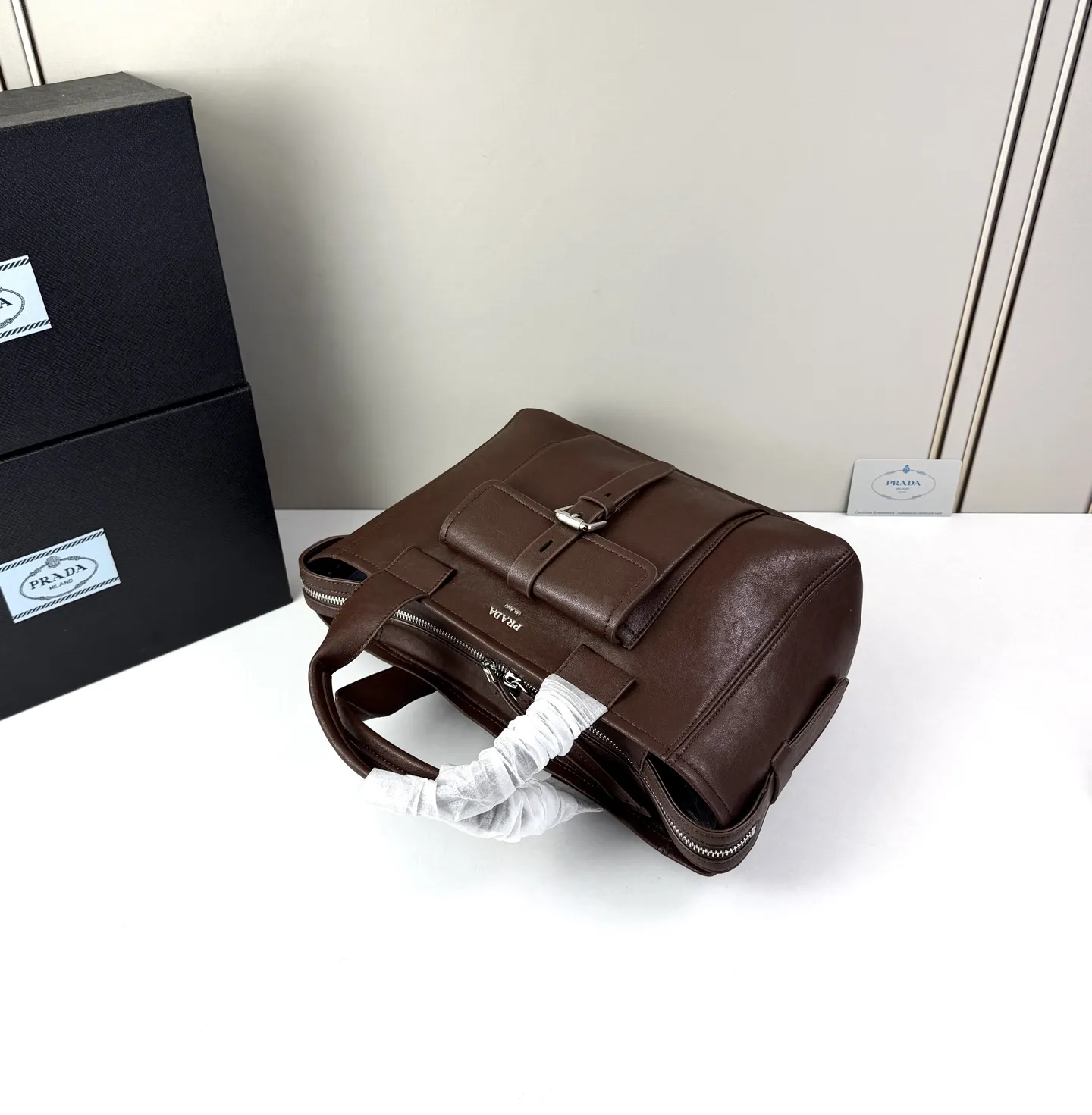 💰280 💥🔥 ​​Prada Route系列托特包​​ 👜采用柔韧耐造的纹理皮革，包身利落的梯形结构，正面设有带扣翻盖口袋，搭配顶部双提手，整体线条硬朗，自带复古机车感。 ‼️​​标志性肩带​​：配备印有 &ldquo;PRADA&rdquo; 字母的宽版织带，可斜挎也可单肩，是Route系列最显著的识别符号，视觉冲击力强 款号：660 尺寸：28&times;21&times;13cm