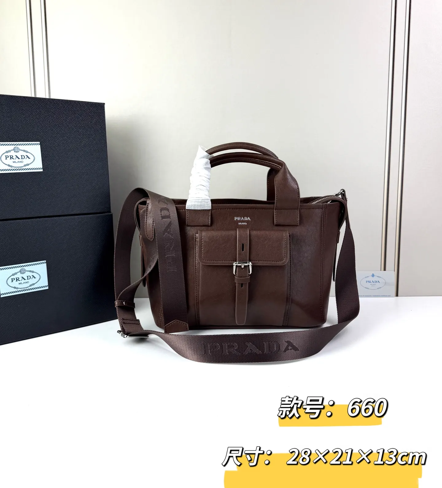 💰280 💥🔥 ​​Prada Route系列托特包​​ 👜采用柔韧耐造的纹理皮革，包身利落的梯形结构，正面设有带扣翻盖口袋，搭配顶部双提手，整体线条硬朗，自带复古机车感。 ‼️​​标志性肩带​​：配备印有 &ldquo;PRADA&rdquo; 字母的宽版织带，可斜挎也可单肩，是Route系列最显著的识别符号，视觉冲击力强 款号：660 尺寸：28&times;21&times;13cm