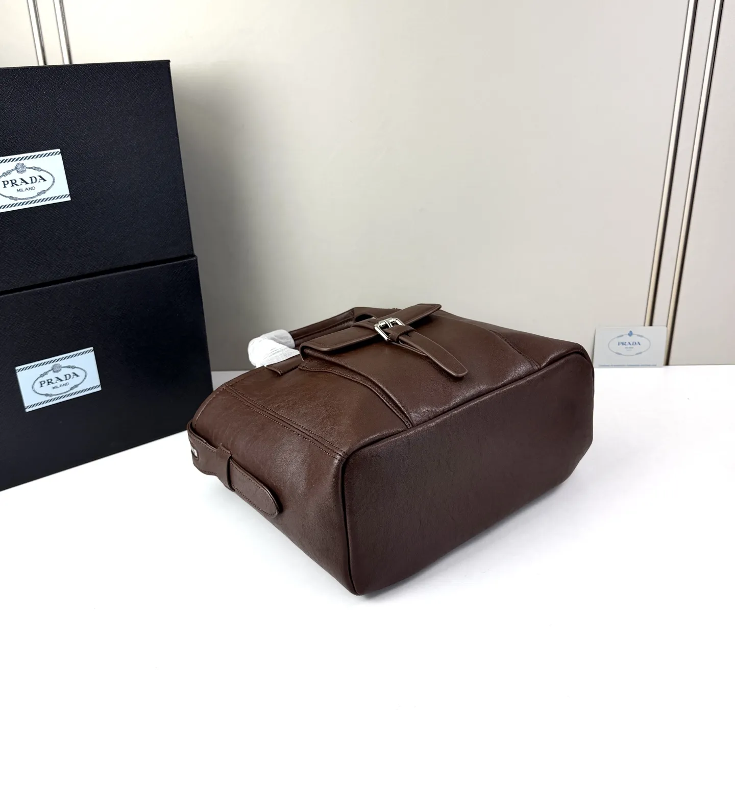 💰280 💥🔥 ​​Prada Route系列托特包​​ 👜采用柔韧耐造的纹理皮革，包身利落的梯形结构，正面设有带扣翻盖口袋，搭配顶部双提手，整体线条硬朗，自带复古机车感。 ‼️​​标志性肩带​​：配备印有 &ldquo;PRADA&rdquo; 字母的宽版织带，可斜挎也可单肩，是Route系列最显著的识别符号，视觉冲击力强 款号：660 尺寸：28&times;21&times;13cm