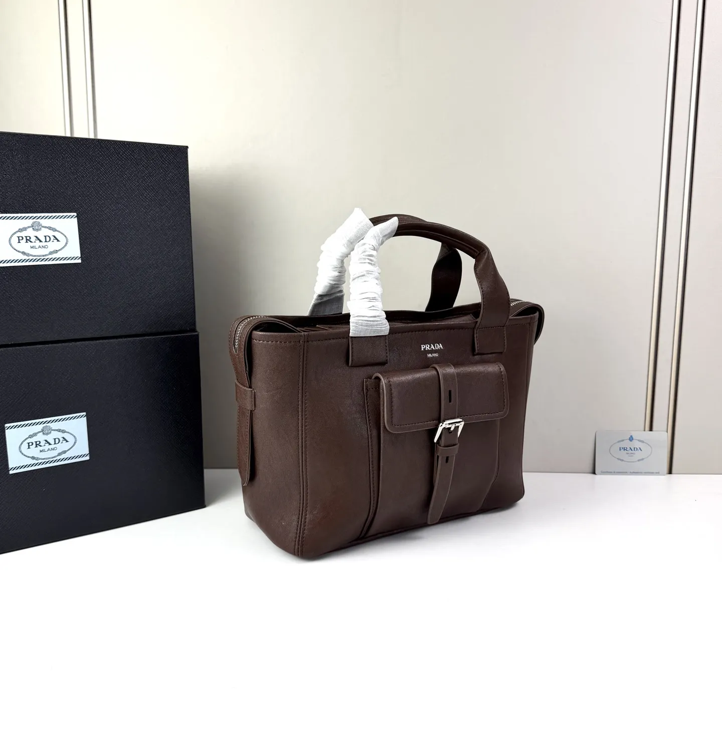 💰280 💥🔥 Prada Route系列托特包 👜采用柔韧耐造的纹理皮革,包身利落的梯形结构,正面设有带扣翻盖口袋,搭配顶部双提手,整体线条硬朗,自带复古机车感。 ‼️标志性肩带:配备印有 “PRADA” 字母的宽版织带,可斜挎也可单肩,是Route系列最显著的识别符号,视觉冲击力强 款号:660 尺寸:28×21×13cm