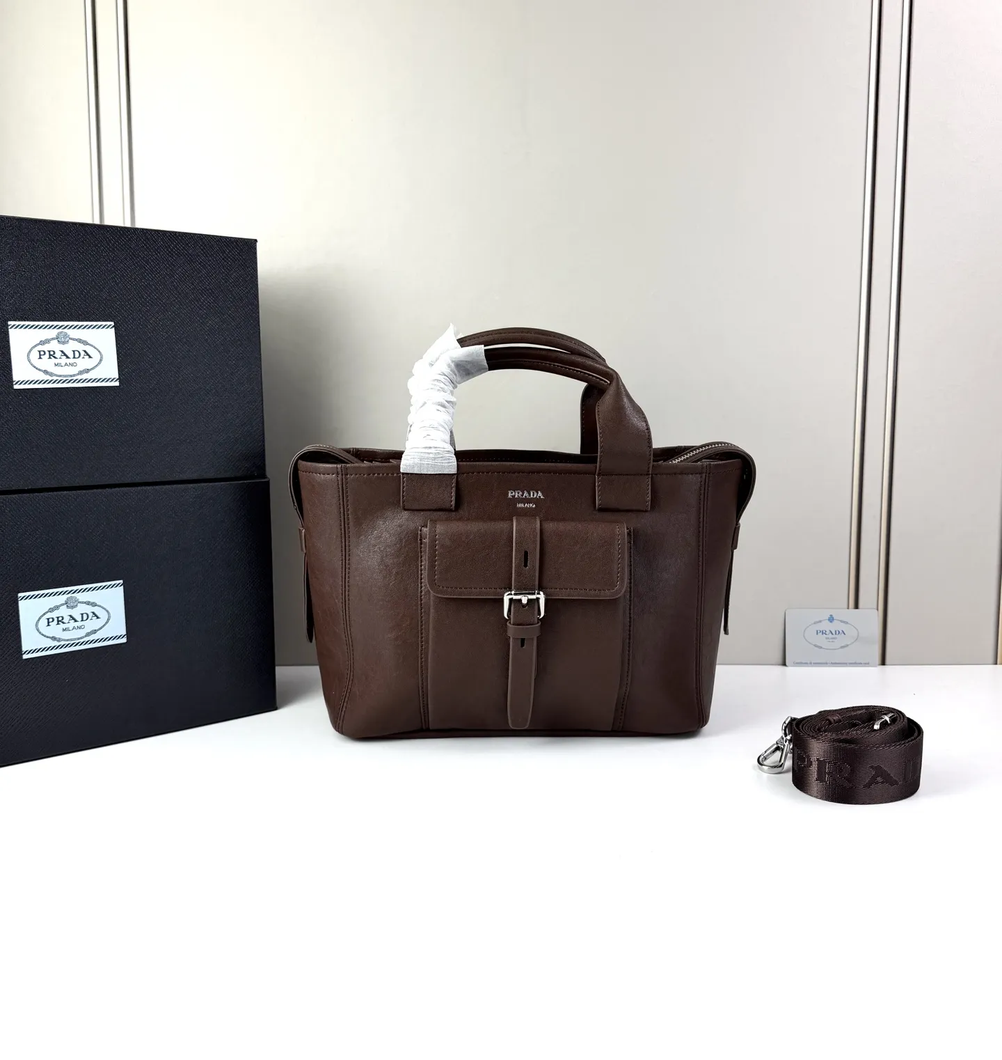 💰280 💥🔥 Prada Route系列托特包 👜采用柔韧耐造的纹理皮革,包身利落的梯形结构,正面设有带扣翻盖口袋,搭配顶部双提手,整体线条硬朗,自带复古机车感。 ‼️标志性肩带:配备印有 “PRADA” 字母的宽版织带,可斜挎也可单肩,是Route系列最显著的识别符号,视觉冲击力强 款号:660 尺寸:28×21×13cm