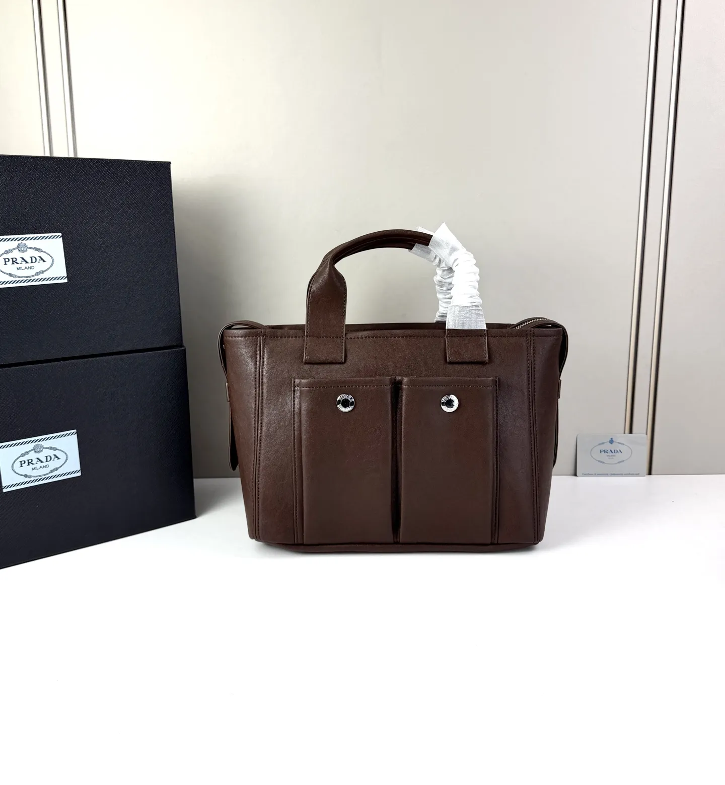 💰280 💥🔥 ​​Prada Route系列托特包​​ 👜采用柔韧耐造的纹理皮革，包身利落的梯形结构，正面设有带扣翻盖口袋，搭配顶部双提手，整体线条硬朗，自带复古机车感。 ‼️​​标志性肩带​​：配备印有 &ldquo;PRADA&rdquo; 字母的宽版织带，可斜挎也可单肩，是Route系列最显著的识别符号，视觉冲击力强 款号：660 尺寸：28&times;21&times;13cm